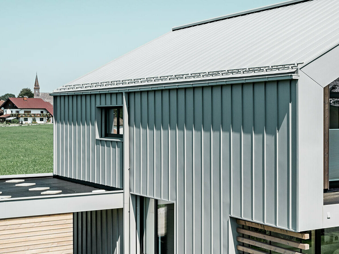 Obiteljska kuća s dvostrešnim krovom, PREFALZ sustavom na krovu i fasadi; za krovnu odvodnju upotrijebljen je PREFA sandučasti žlijeb s PREFA kvadratnom cijevi u posebnoj patina sivoj boji.