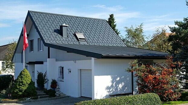 Sanirana kuća s dvostrešnim krovom na koji se nastavlja garaža. Krov je pokriven PREFA krovnom pločom, a garaža Prefalz-om u antracit boji. Ispred kuće je jarbol sa švicarskom zastavom.
