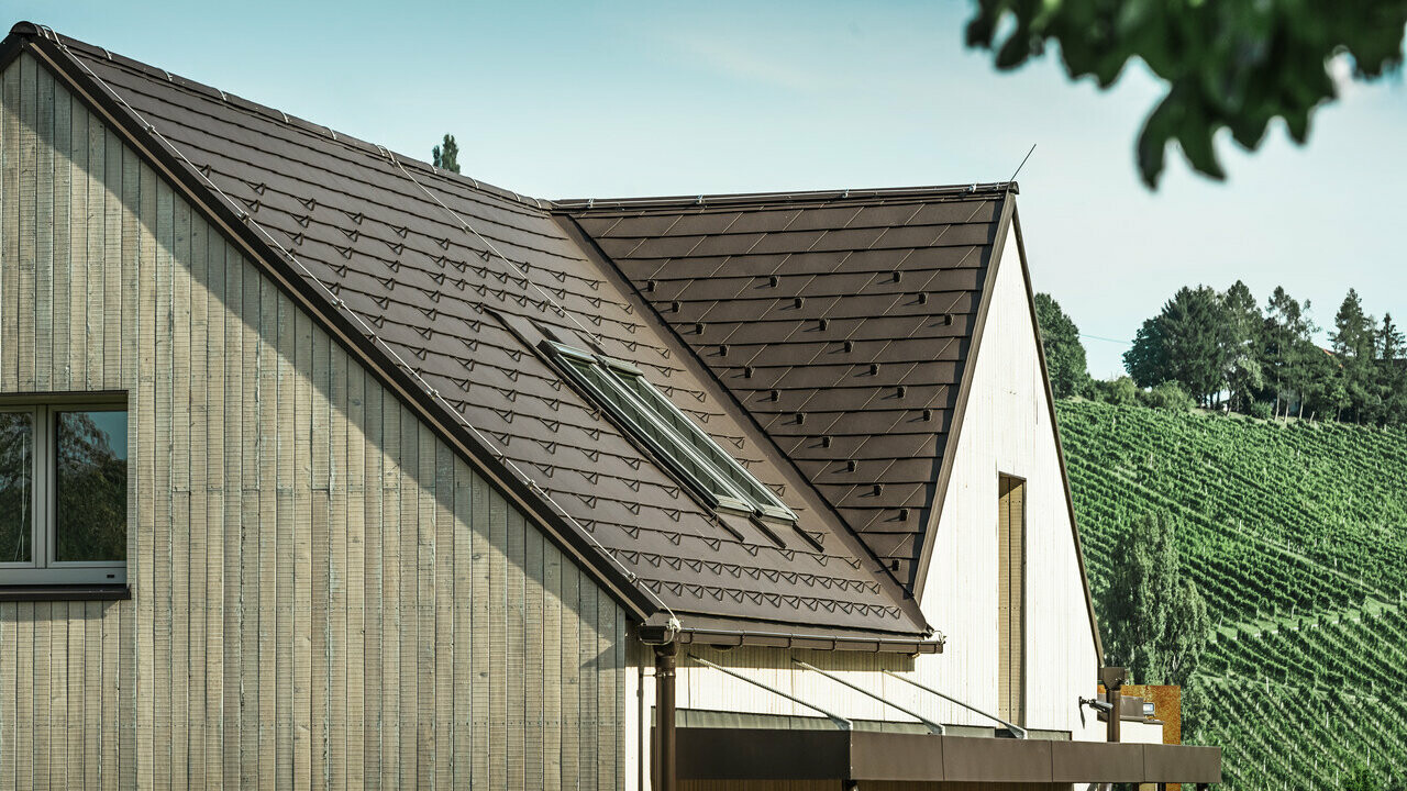 Jednoobiteljska kuća s dva dvostrešna krova pokrivena je PREFA krovnom šindrom u orah smeđoj boji. Krovna odvodnja vrši se preko PREFA sandučastog žlijeba. Fasada je obložena istrošenim drvetom.