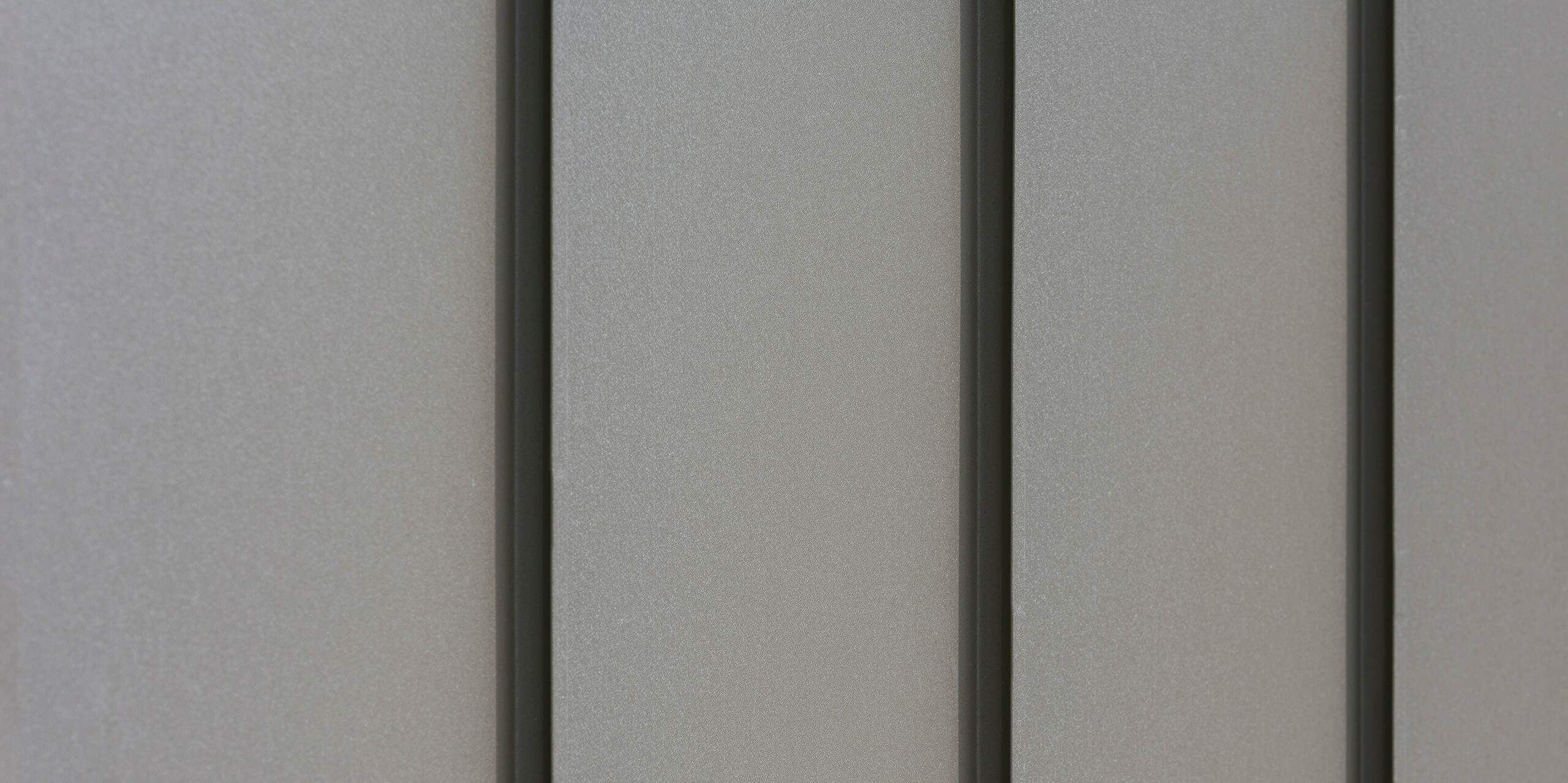 Nahaufnahme einer modernen Fassadenverkleidung aus Aluminium mit vertikalen Scharen, die für ein ästhetisch strukturiertes Muster sorgen. Das Aluminium kommt von der PREFA Aluminiumprodukte GmbH.