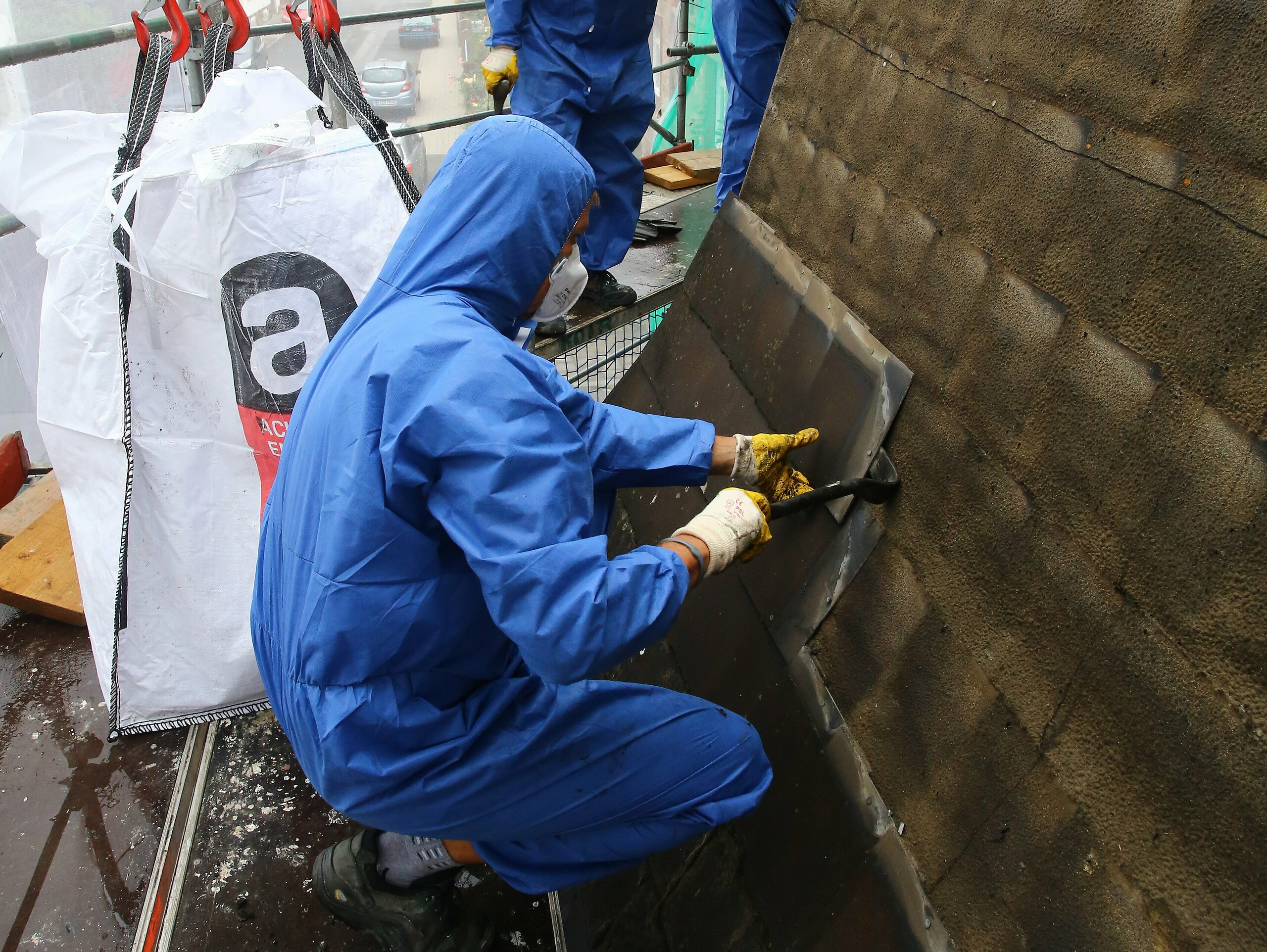 Geschulter Arbeiter beim Entfernen und Entsorgen der asbesthältigen, alten Dacheindeckung mit Mundschutz, um ein Einatmen des Asbests zu vermeiden
