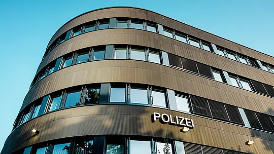 Dramatičan pogled ispod zakrivljenog novog dijela Policijske postaje 43 u Hamburgu otkriva upečatljivu PREFA aluminijsku fasadu od eloksiranih ekstrudiranih zupčastih profila u srednje brončanoj nijansi. Kao snažan arhitektonski element, fasada privlači pažnju svojom finom, ritmičnom strukturom koja stvara dinamičnu igru svjetla i sjene te naglašava fluidne zaobljene oblike građevine. PREFA aluminij pruža izvrsnu otpornost na vremenske uvjete i koroziju, iznimnu dugotrajnost te predstavlja održivo rješenje s minimalnim zahtjevima za održavanje za precizno oblikovane, suvremene fasade.