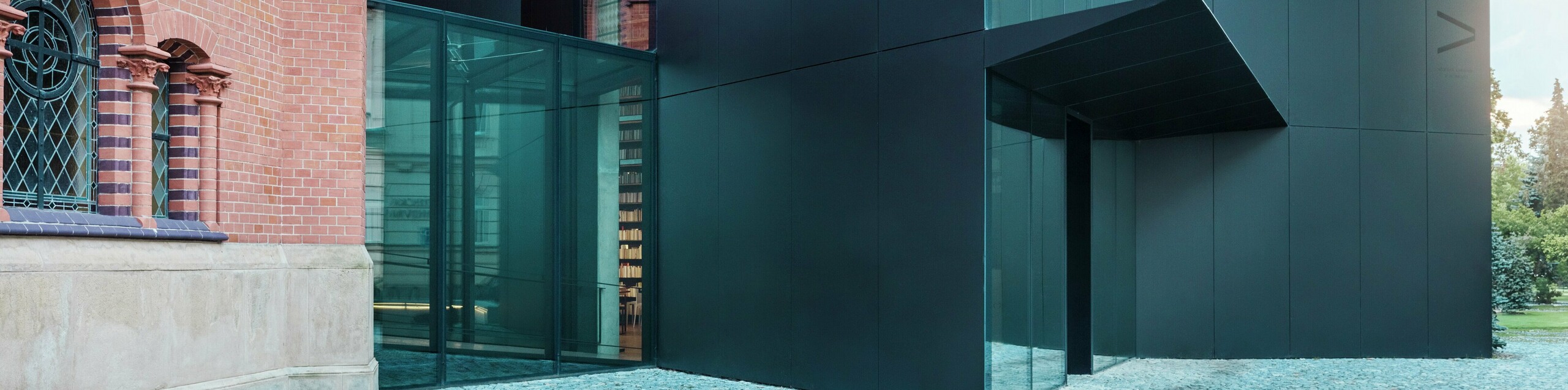 Slika prikazuje modernu nadogradnju knjižnice koja se elegantno nadovezuje na povijesnu Crvenu crkvu u Olomoucu. Zapanjujući novi objekt impresionira fasadom od crnih PREFABOND aluminijsko-kompozitnih ploča, oblikovanih u čistim, geometrijskim linijama i izrađenih s preciznom pažnjom na detalje. Stakleni zidovi zgrade omogućuju transparentan pogled u unutrašnjost, koja se skladno uklapa u povijesno okruženje. Igra modernih materijala i klasičnih arhitektonskih elemenata stvara zanimljivu vizualnu povezanost između starog i novog. Inovativna primjena PREFABOND ploča osigurava ne samo moderan izgled, već i dugovječnost i otpornost, pripremajući zgradu za budućnost.