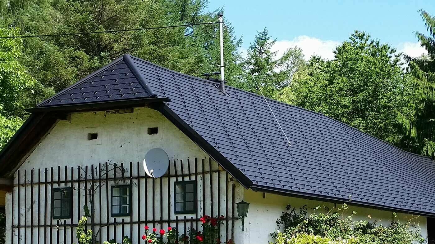 Altes traditionelles Bauernhaus mit Krüppelwalmdach; Das Dach wurde mit der Aluschindel in Schwarz von PREFA neu eingedeckt, an der Fassade ranken sich Kletterpflanzen hoch.