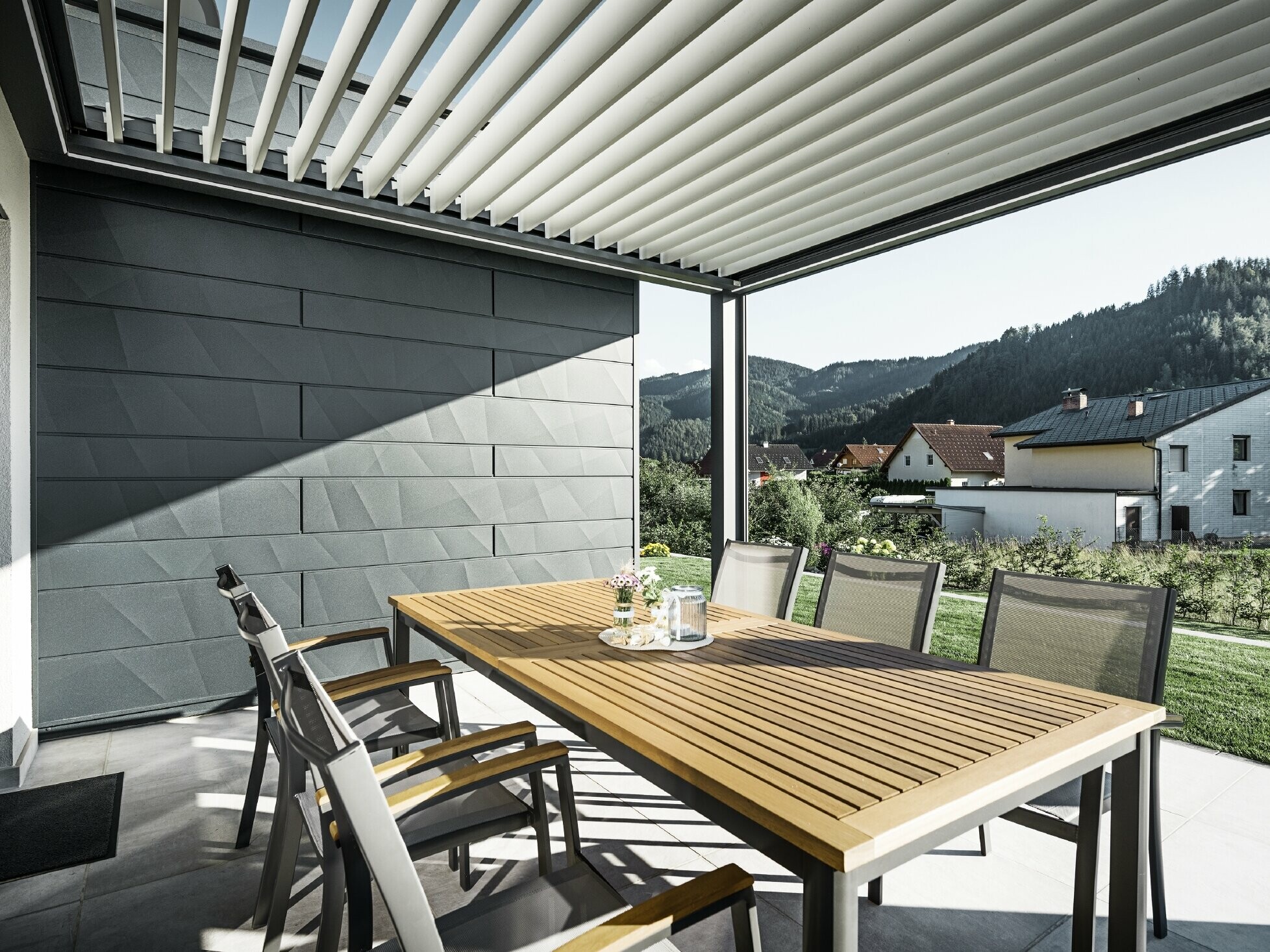 Zaštićena terasa natkrivena lamelama, sa stolom i stolicama; jedna strana fasade obložena je PREFA fasadnim panelima kazeta.X u antracit boji.