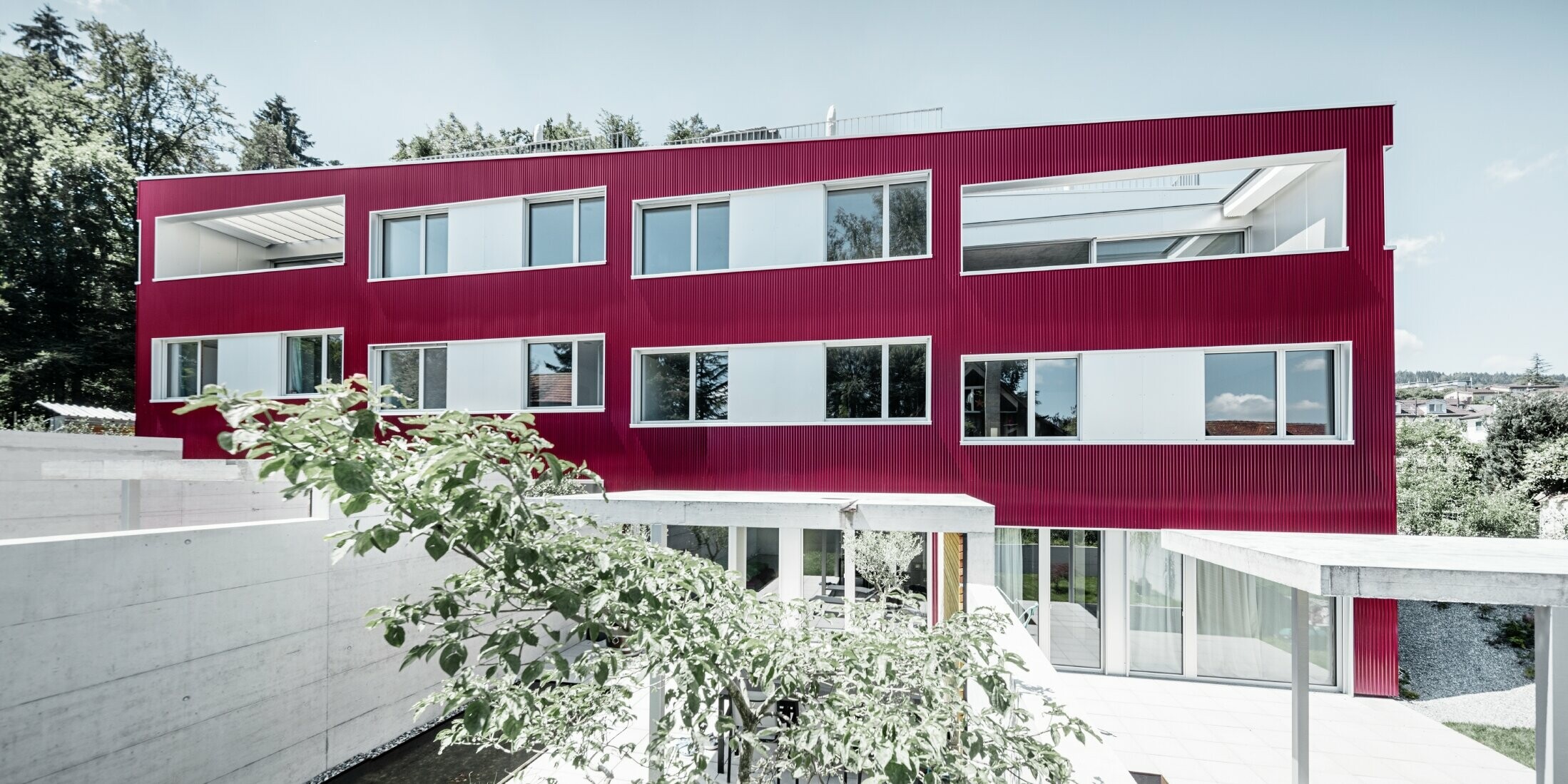 Stambeni kompleks s ravnim krovom i balkonima s fasadom u crvenoj boji vina s PREFA valovitim profilom 