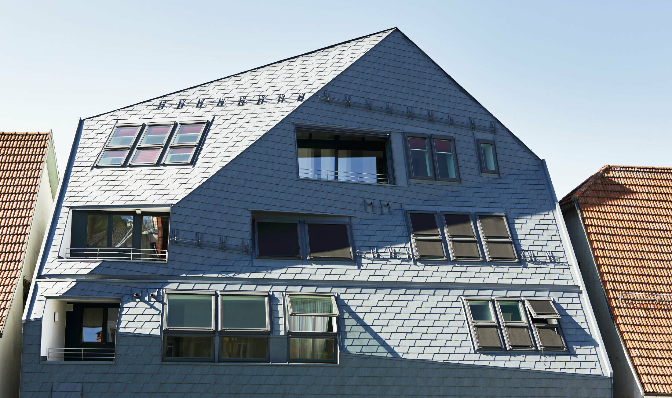 Galerijska kuća s prelomljenom fasadnom površinom, obložena s PREFA krovnom i zidnom šindrom u P.10 kameno sivoj boji s dosta prozora