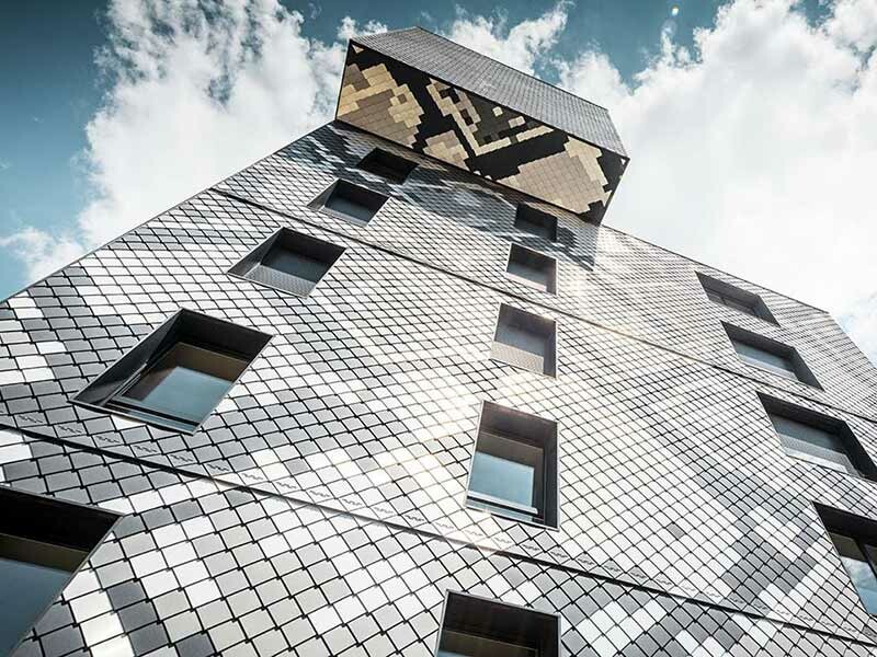 Pogled s podnožja zgrade Le Python u Grenobleu, obložene PREFA aluminijskim zidnim rombom 20 × 20 u bojama antracit, svijetlo siva, prirodni aluminij i srebrna metalik, nebo je malo oblačno