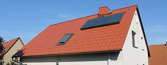 Obiteljska kuća s dvostrešnim krovom pokrivenim PREFA krovnom pločom u ciglasto crvenoj. Krovna površina sa solarnim panelima i krovnim prozorom