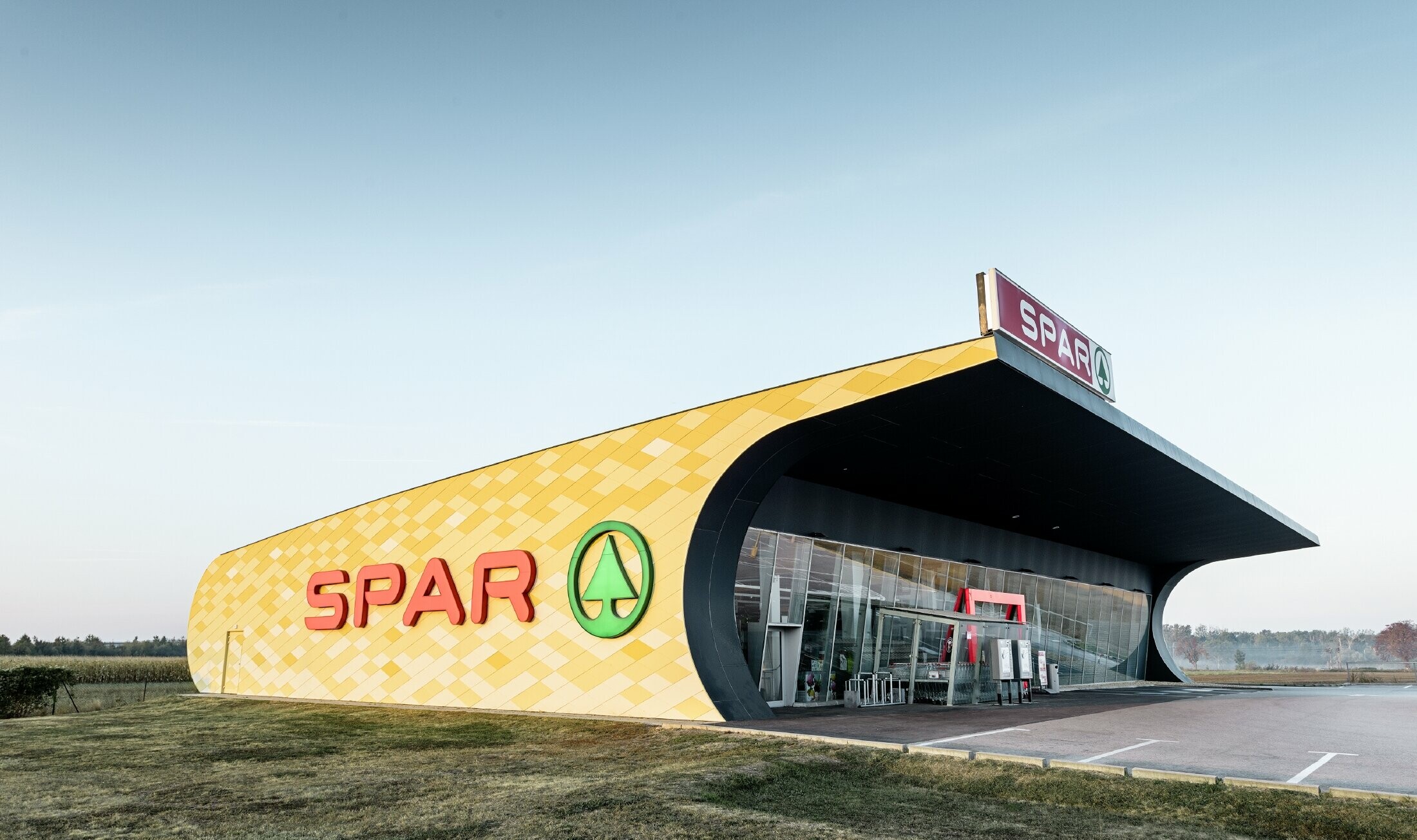 Spar podružnica s kariranom aluminijskom fasadom u žuto-narančastoj boji i Spar Logotipom