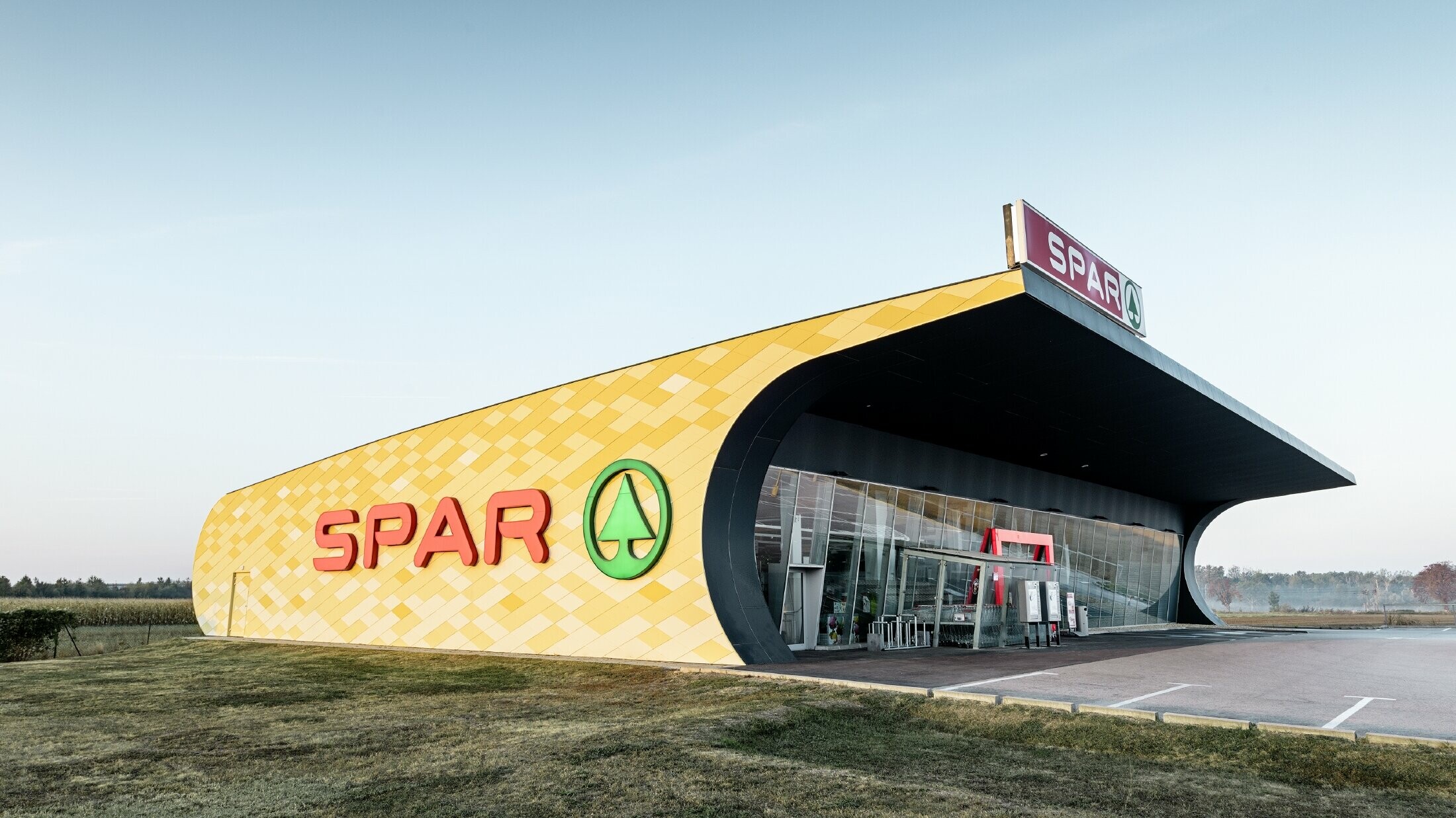 Spar podružnica s kariranom aluminijskom fasadom u žuto-narančastoj boji i Spar Logotipom