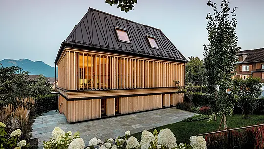 Moderno „Badehaus“ hotela Hirschen u Schwarzenbergu ima nagrađivani PREFA krov s falcom u boji P.10 orah smeđa. Ikonični krov s četiri vode, nagiba 60 stupnjeva i nekonvencionalno postavljenim falcima, predstavlja arhitektonsko remek-djelo koje spaja tradiciju i inovaciju. Fasada od vertikalnih drvenih lamela daje zgradi toplu, prirodnu pojavu i skladno se uklapa u zaštićeno središte mjesta. PREFALZ oduševljava dugovječnošću, slobodom oblikovanja i izvrsnom obradivošću, čak i kod složenih krovnih oblika. Nagrađivani primjer inovativne arhitekture s visokokvalitetnim PREFA proizvodima.
