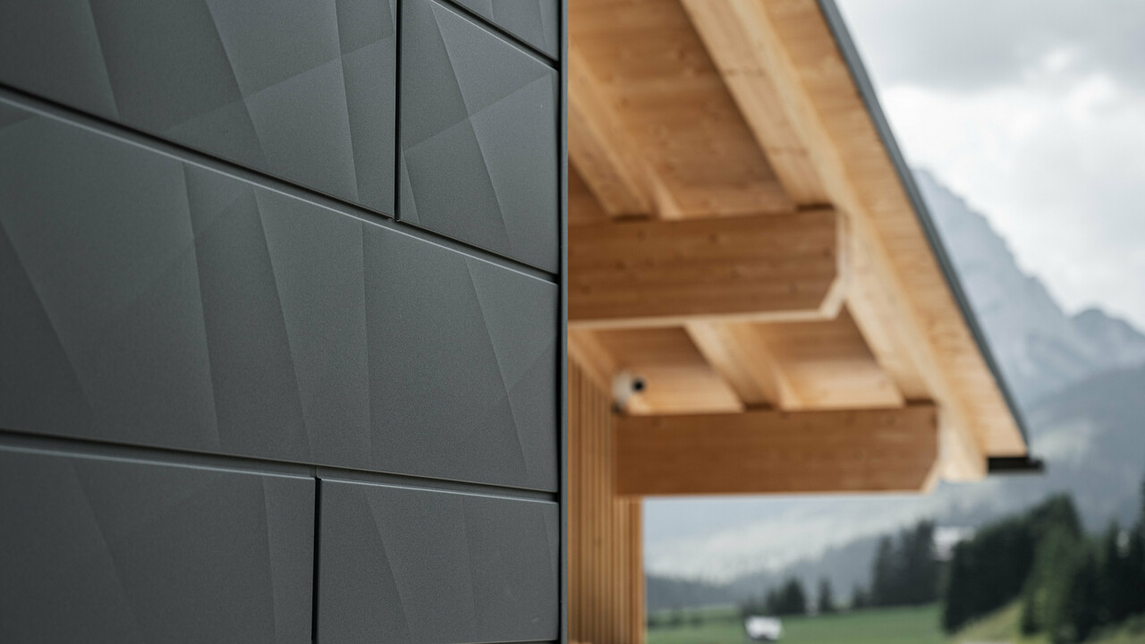 Krupni kadar PREFA fasadnog panela fasadna kazeta.X u P.10 crnoj boji na objektu Casa Hoffe u mjestu Sappada, Italija. Aluminijski fasadni sustav vješto je ukomponiran u moderni, apstraktni dizajn koji stvara atraktivan kontrast vidljivim drvenim elementima krovišta. Inovativno fasadno rješenje besprijekorno se uklapa u alpski pejzaž i predstavlja spoj funkcionalnosti, otpornosti i građevinske kulture vođene estetikom.