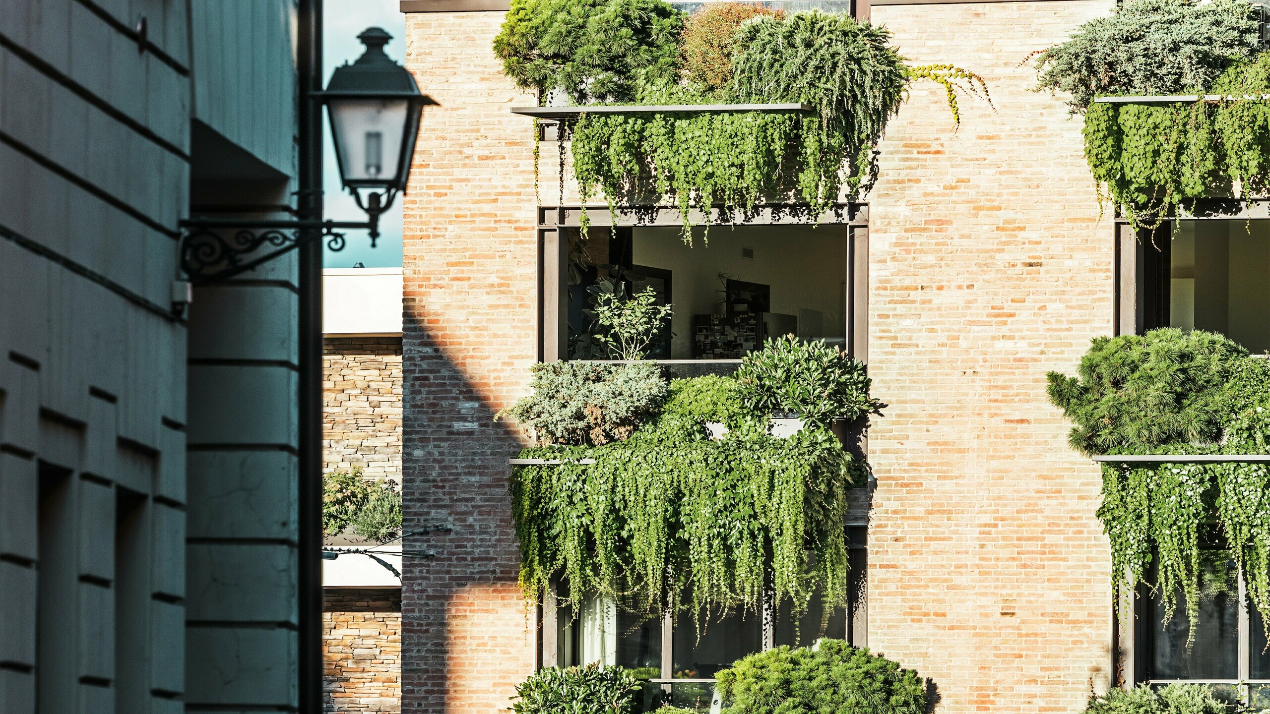 Detailansicht einer begrünten Backsteinfassade in Italien mit hängenden Gärten, PREFALZ Architekturdetails und angrenzender Altstadtumgebung mit Laterne.