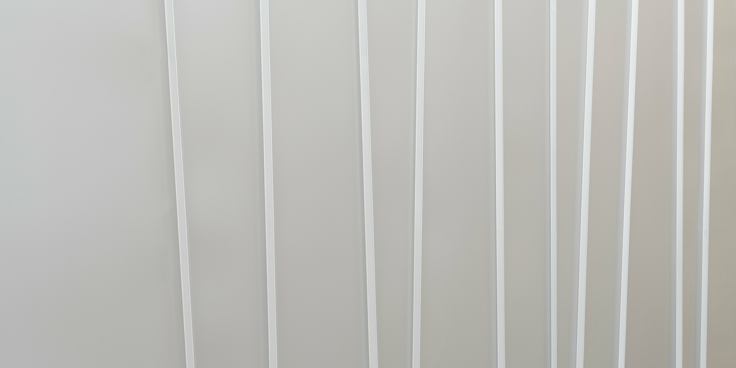 Nahaufnahme eines modernen Fassadensystems aus PREFALZ in Hellgrau mit verschiedenen Scharenbreiten. Die klare und minimalistische Textur vermittelt ein Gefühl von Ordnung und zeitgemäßem Design.