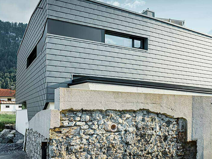 Fasadna obloga s PREFA zidnom šindrom od aluminija u svijetlo sivoj s kamenim zidom ispred kuće