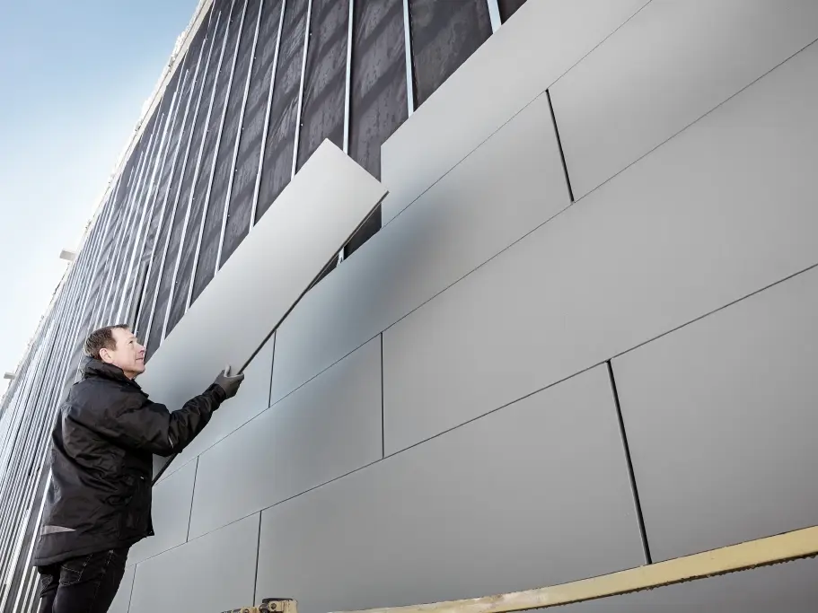 Fotografije djelomično dovršene fasade obložene PREFA fasadnim kazetama širine 500. Limar polaže novi fasadni panel. Fotografija je slikana odozdo. 