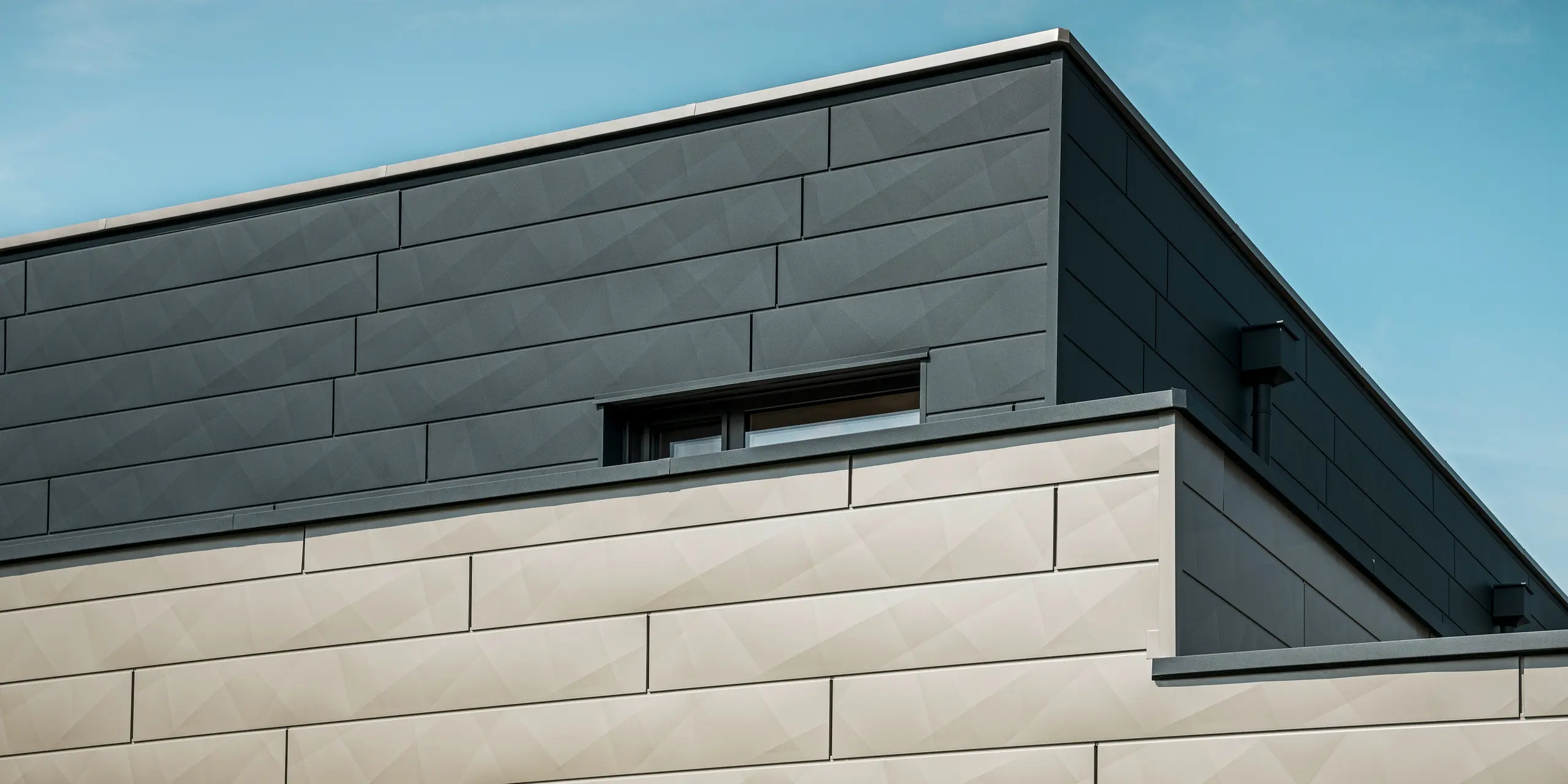 [Translate to Hrvatski:] Nahaufnahme der zweifarbigen PREFA Aluminiumfassade eines modernen Einfamilienhauses in Wippenham, Österreich. Die Fassade ist mit Siding.X Fassadenpaneelen in den Farben Anthrazit und Bronze gestaltet, die ein elegantes und dynamisches Erscheinungsbild erzeugen. Die präzise Verarbeitung und das Zusammenspiel der Farben betonen die zeitgemäße Architektur des Gebäudes.