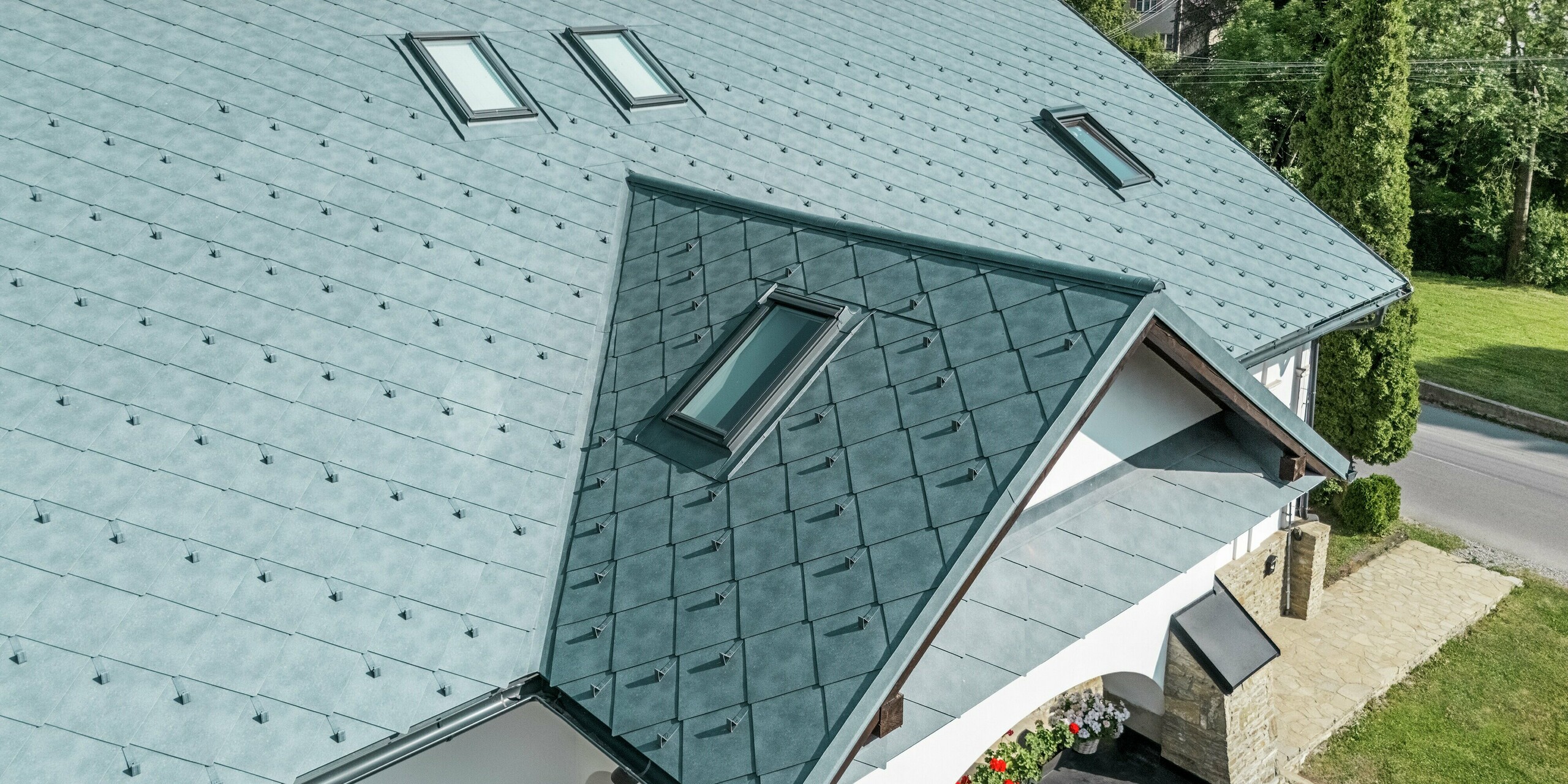 Das Bild zeigt das sanierte Dach eines historischen Handwerkerhauses in Klin, Slowakei, eingedeckt mit der PREFA Dachraute 44 × 44 in P.10 Steingrau. Die markanten Rauten verleihen dem Gebäude einen eleganten, modernen Charakter, ohne den traditionellen Charme zu verlieren. Besonders ins Auge fallen die gleichmäßige Struktur der Dachdeckung, die harmonische Farbwirkung und die stilvoll integrierten Dachfenster. Das Aluminiumdach überzeugt nicht nur optisch, sondern auch durch seine Vorteile: Es ist extrem langlebig, leicht, wetterfest und korrosionsbeständig. Damit wird die Sanierung zu einem nachhaltigen Projekt, das Schönheit und Funktion perfekt vereint.