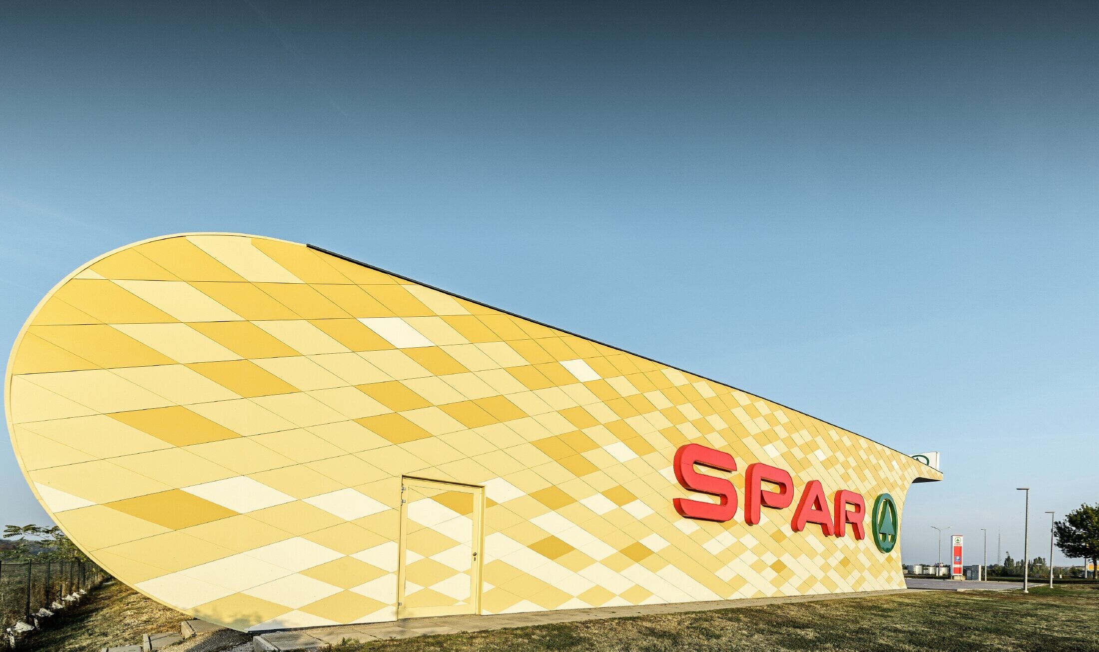 Spar podružnica s kariranom aluminijskom fasadom u žuto-narančastoj boji i Spar Logotipom