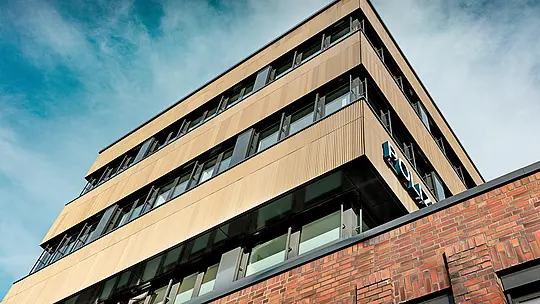 Dinamičan pogled ispod Policijske postaje 43 u Hamburgu otkriva jasno oblikovanu novogradnju s PREFA aluminijskom fasadom od ekstrudiranih zupčastih profila u elegantnoj srednje brončanoj nijansi. Fino rebrasta površina djeluje kao snažan vizualni element, stvarajući zanimljivu igru svjetla i sjene duž horizontalnih prozorskih nizova. U kontrastu s masivnom opečnom arhitekturom nastaje upečatljiv i prepoznatljiv arhitektonski izraz. PREFA aluminij pruža izvrsnu otpornost na koroziju, dug vijek trajanja i minimalne zahtjeve za održavanje – idealno rješenje za održivo i precizno oblikovane fasadne koncepte.