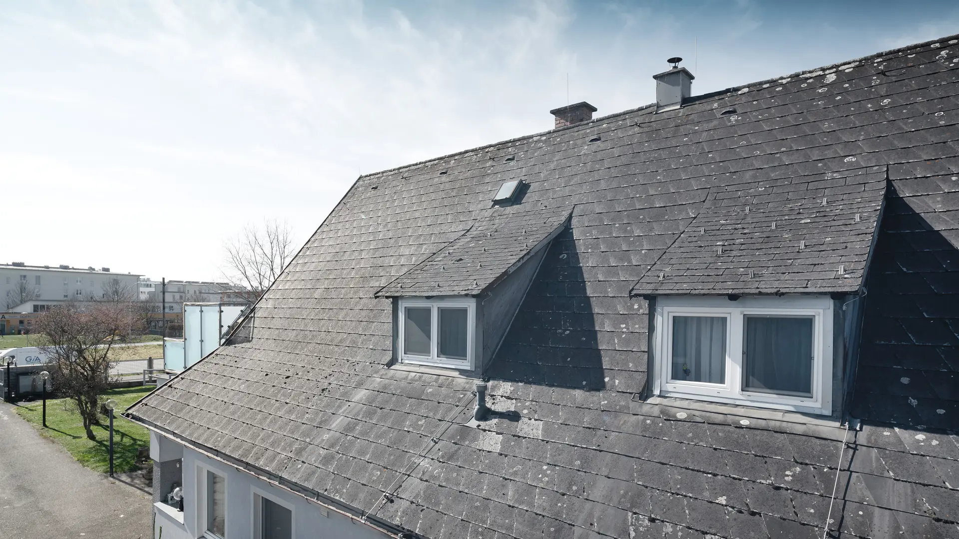 Krupni plan starog Eternit krova koji pokazuje znakove habanja i rasta lišaja. Na krovu su vidljiva dva šilca. Fotografija snimljena prije obnove krova.