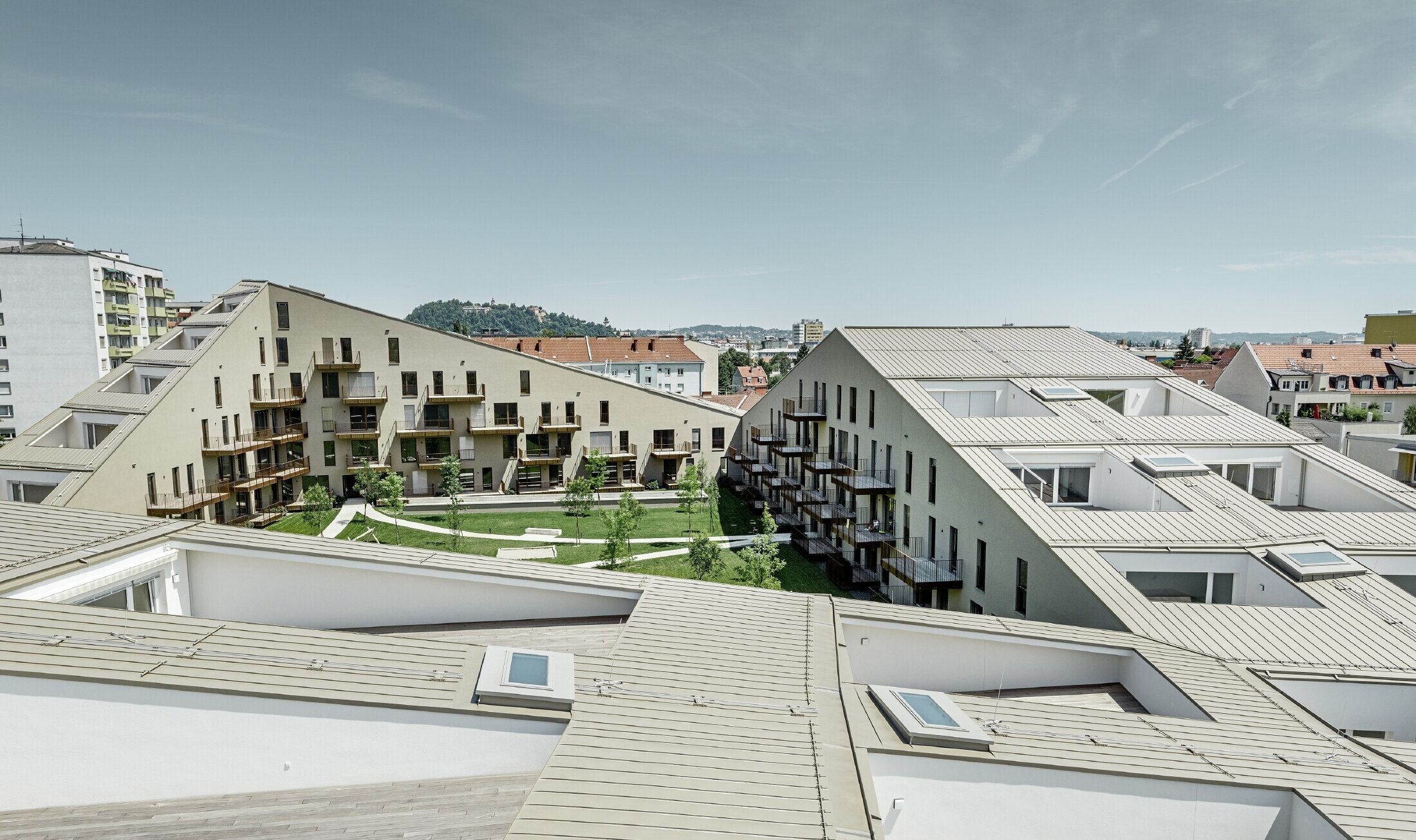 Izduženo stambeno naselje u Grazu s krovnim površinama blagog nagiba, s integriranim terasama i velikoplošnim prozorima i s krovnim pokrovom iz Prefalza u specijalnoj boji bronce metalik
