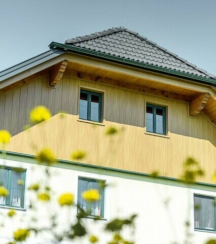 Obloga zabata s aluminijskim panelima tvrtke PREFA u optici drva (prirodni hrast), oblaganje fasadnim kazetama Siding izvedeno je vertikalno te također obuhvaća podsvođe krova