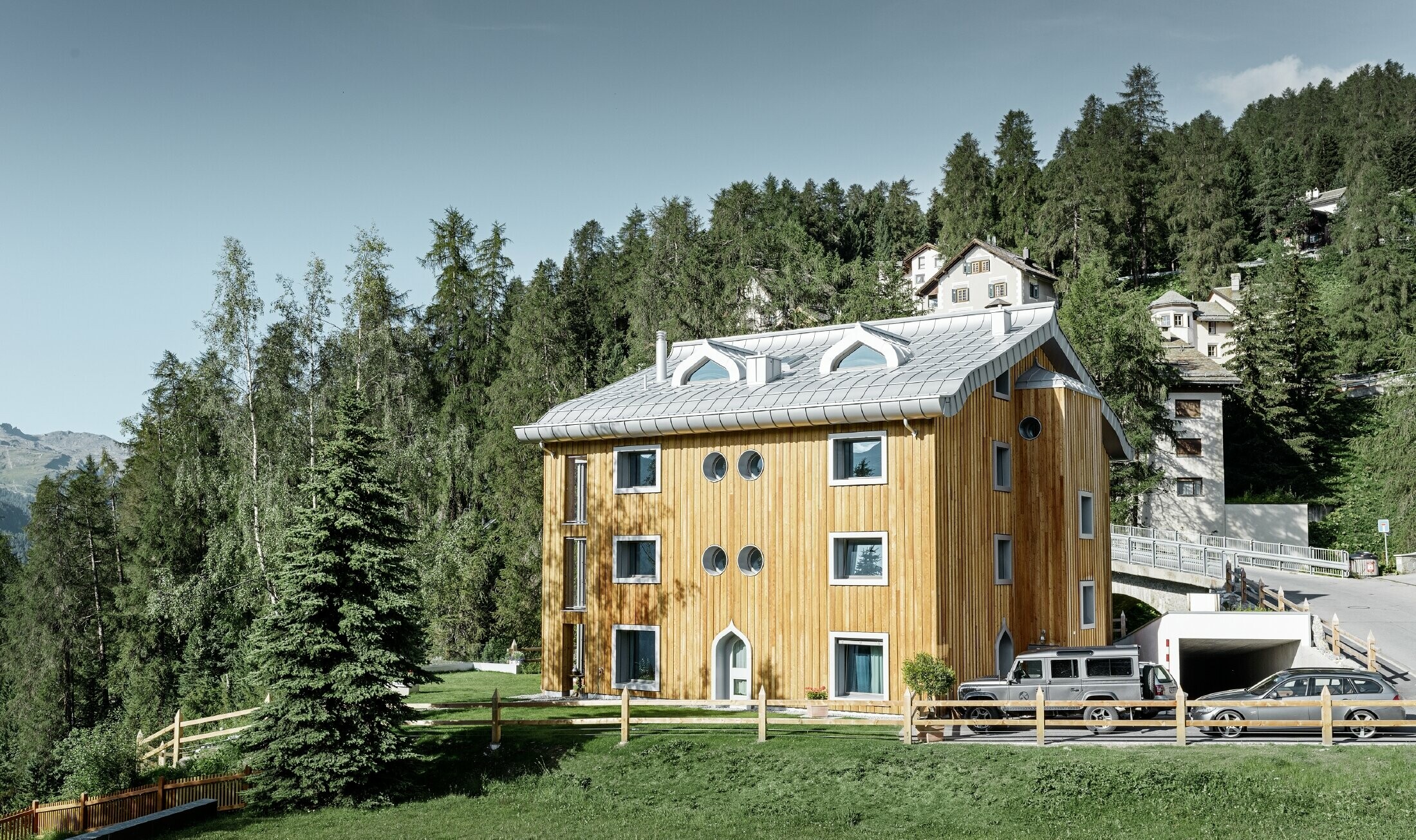Stambeno naselje u St. Moritzu s drvenom fasadom i aluminijskim krovom s lučnom strehom u srebrnoj metalik boji
