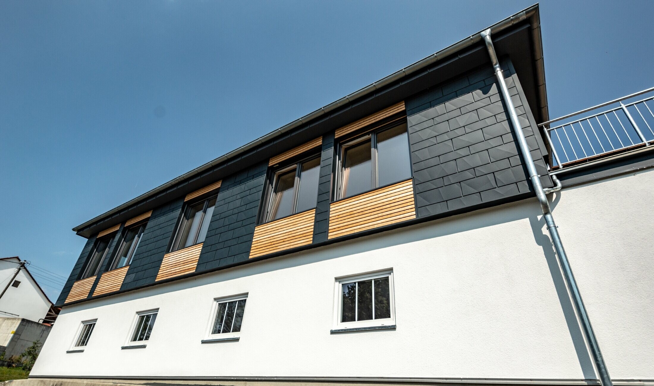 Oblikovanje fasada s različitim građevinskim materijalima: korišteni su aluminijski PREFA element Siding.X u antracit boji, horizontalna drvena fasada i bijela žbukana fasada.