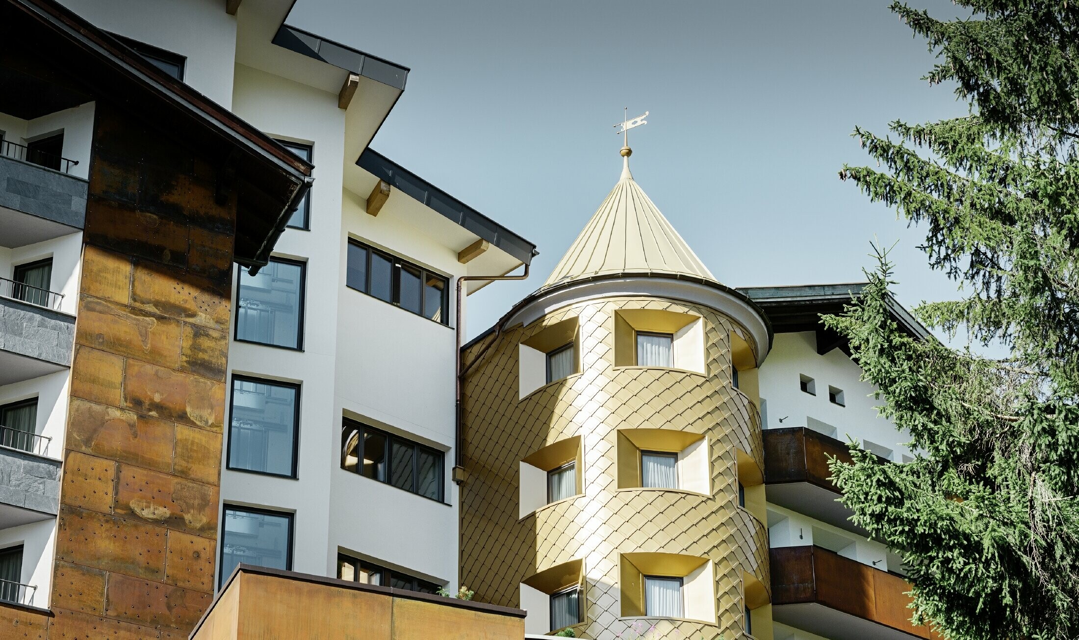 Tradicionalni hotel u Ischglu s drvenim balkonima, drvenom fasadom i tornjem sa zlatnim aluminijskim rombovima od PREFE