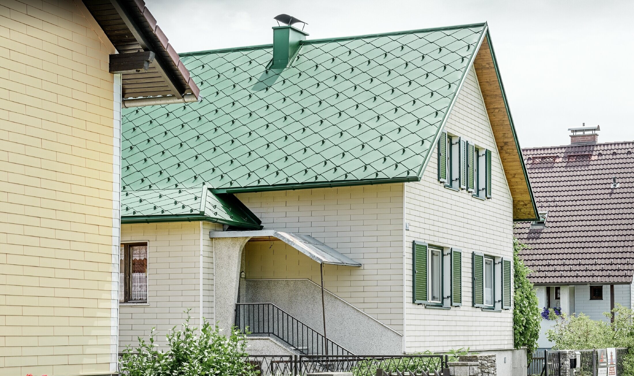 Klasična obiteljska kuća s dvostrešnim krovom i aluminijskim pokrovom od PREFE u mahovinasto zelenoj boji, sa zelenim prozorskim kapcima