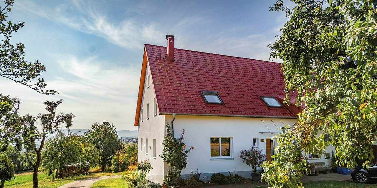 Romantična kućica na selu s puno drveća i grmlja. Pokrivena PREFA krovnom pločom u oksid crvenoj.