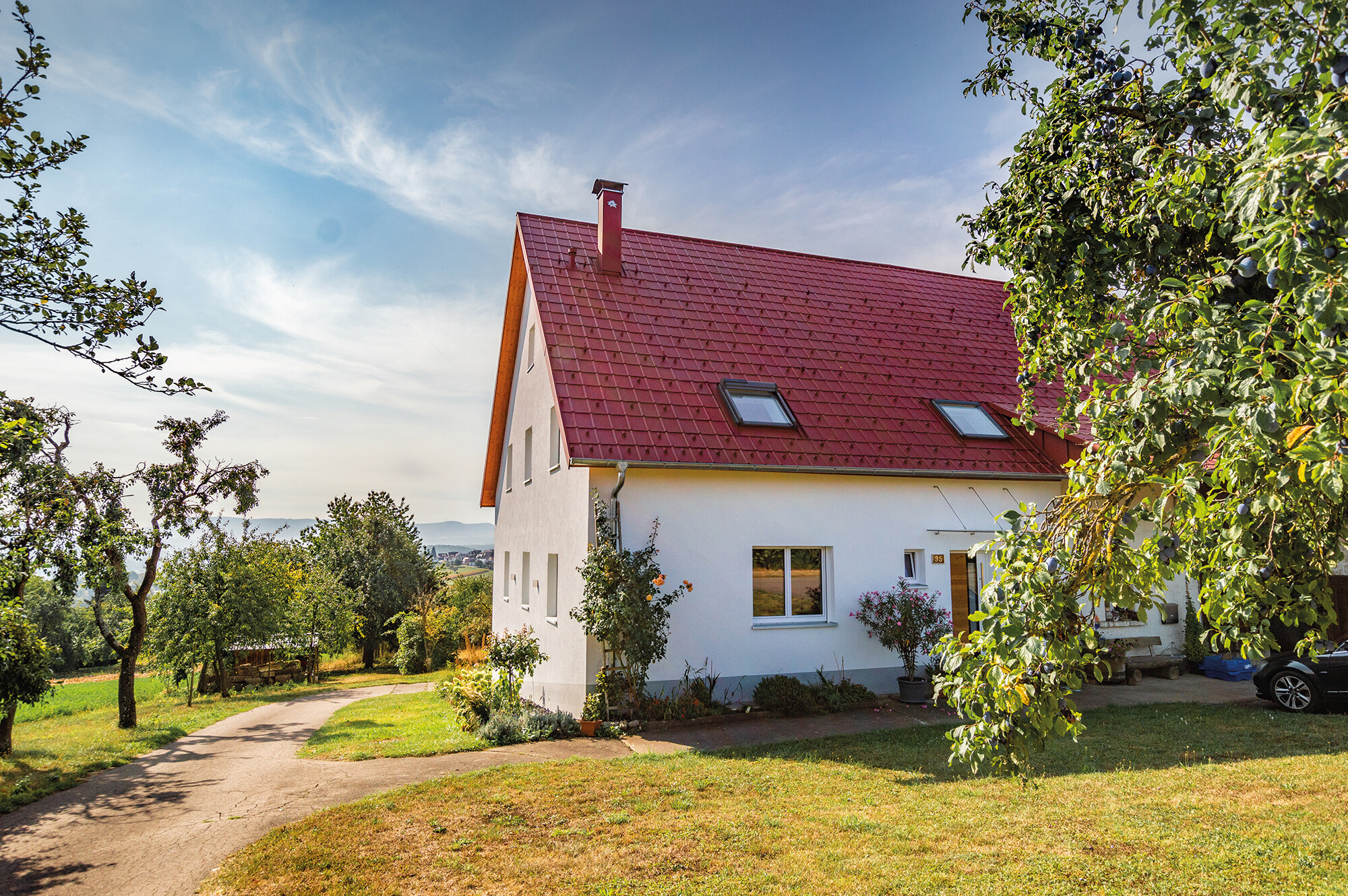 Romantična kućica na selu s puno drveća i grmlja. Pokrivena PREFA krovnom pločom u oksid crvenoj.