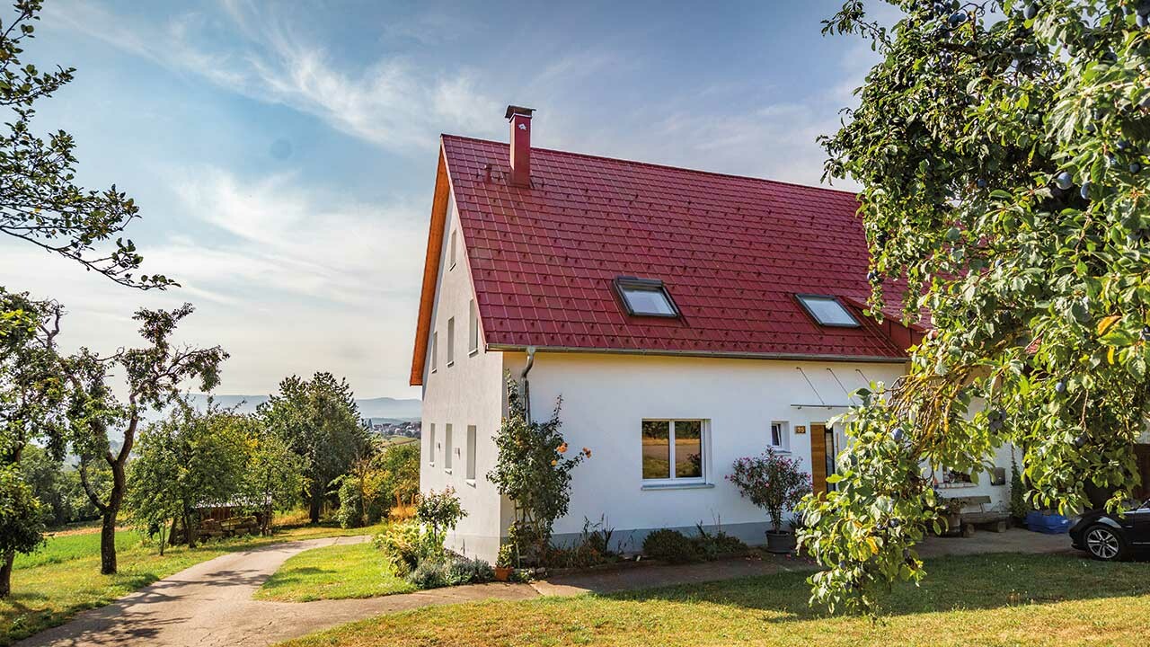 Romantična kućica na selu s puno drveća i grmlja. Pokrivena PREFA krovnom pločom u oksid crvenoj.