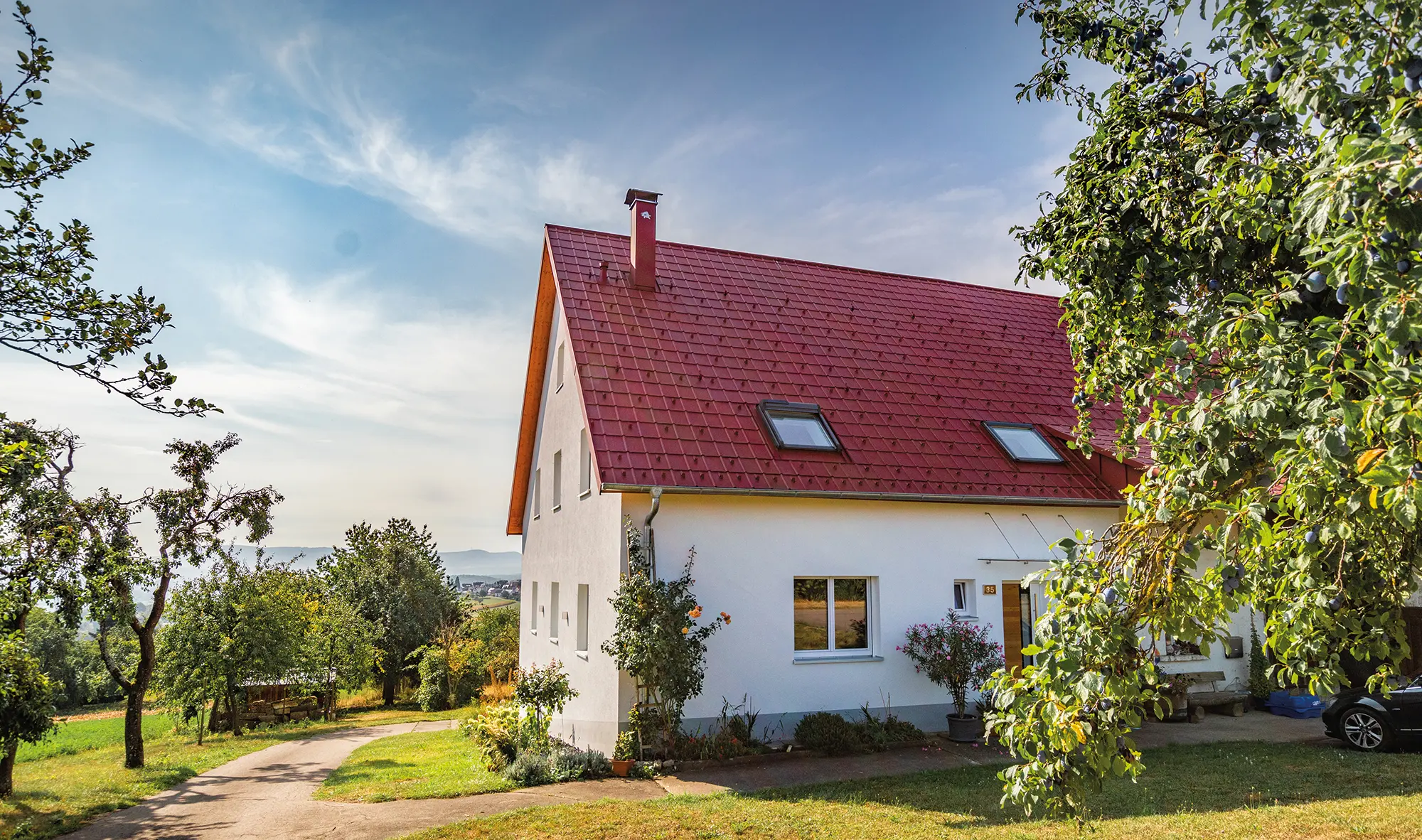 Romantična kućica na selu s puno drveća i grmlja. Pokrivena PREFA krovnom pločom u oksid crvenoj.