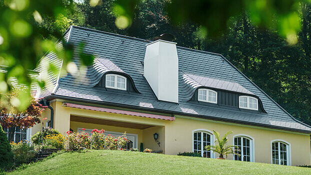 Obiteljska kuća s novo saniranim krovom s PREFA krovnom šindrom u antracit boji sa zaobljenim krovnim kućicama (zakrivljena krovna kućica) i bijelim dimnjakom.