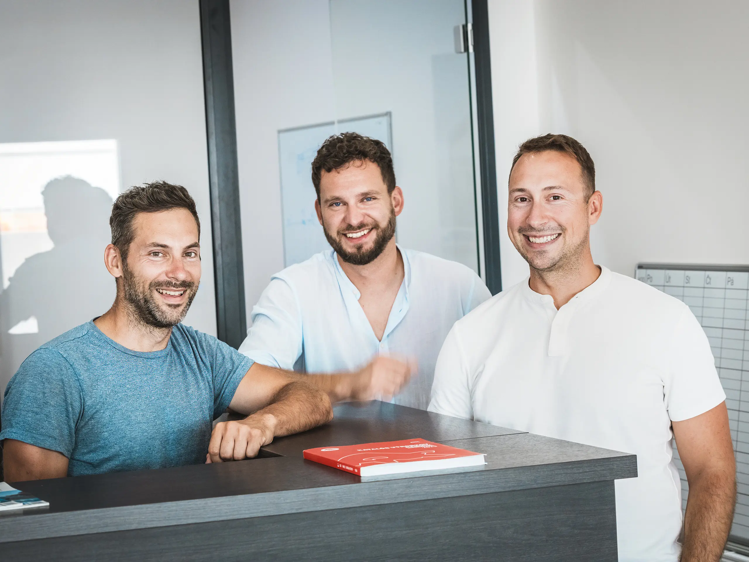 Za recepcijskim pultom u modernom uredu nalaze se braća Juraj i Peter Pekár te Tomáš Filo iz limarske tvrtke Prvá Strechárska, koji pružaju autentičan uvid u projektni tim iza gradske četvrti Vydrica u Bratislavi. Kao ključni sudionici realizirali su složene krovne strukture s PREFA aluminijskim krovnim šindrama, koje se ističu preciznošću, dugotrajnošću i otpornošću na vremenske uvjete te značajno doprinose kvalitetnoj i održivoj građevinskoj ovojnici četvrti.