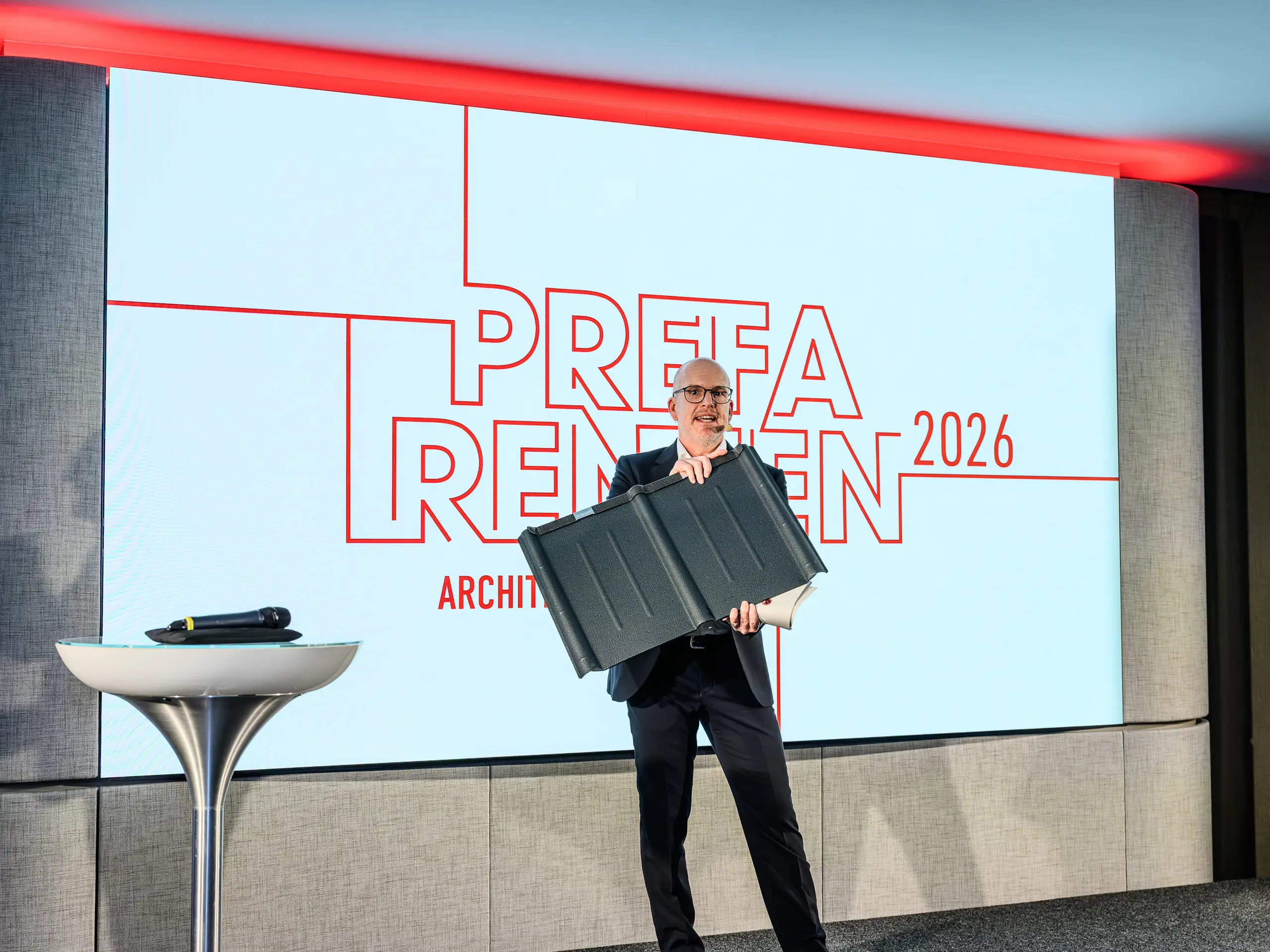 Trenutak vrhunca PREFARENZEN prezentacije 2026.: Jürgen Jungmair, međunarodni direktor marketinga PREFA-e, ponosno predstavlja legendarnu PREFA krovnu ploču. U fokusu je dugotrajni aluminijski proizvod koji se uspješno proizvodi već oko 80 godina. Moderna pozornica s upečatljivim PREFARENZEN logotipom naglašava važnost proizvoda za arhitekturu usmjerenu prema budućnosti. Laka, otporna na oluje, nehrđajuća – PREFA krovna ploča spaja vrhunsku tehniku i estetiku.