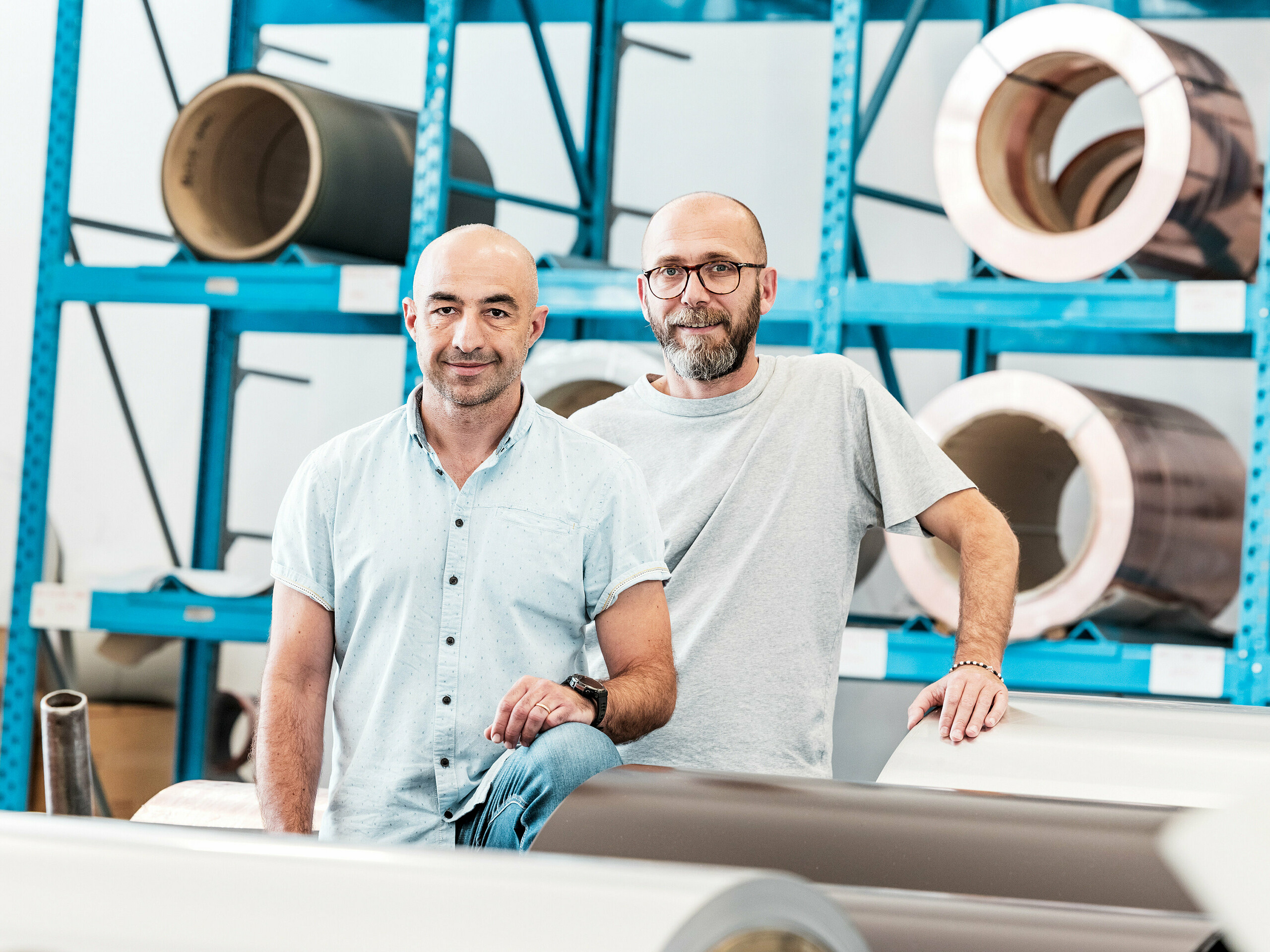 Dva majstora u skladištu aluminija ispred namotanih metalnih zavojnica – moderno radno okruženje za krovne i fasadne sustave od aluminija.
