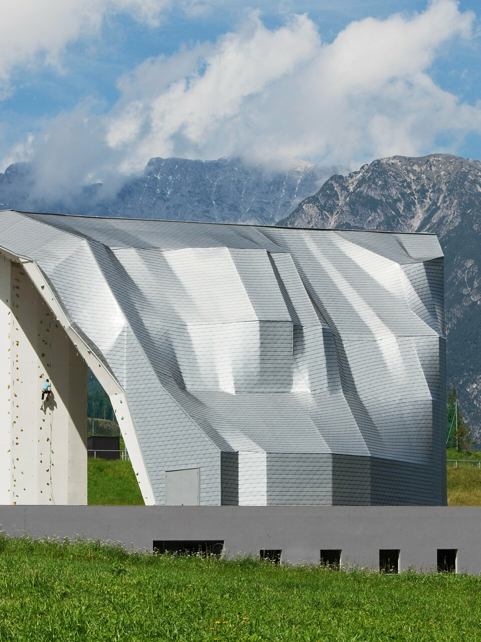 Blick aus der Distanz auf Kletterturm Imst mit PREFA Aluminiumfassade und Bergpanorama im Hintergrund