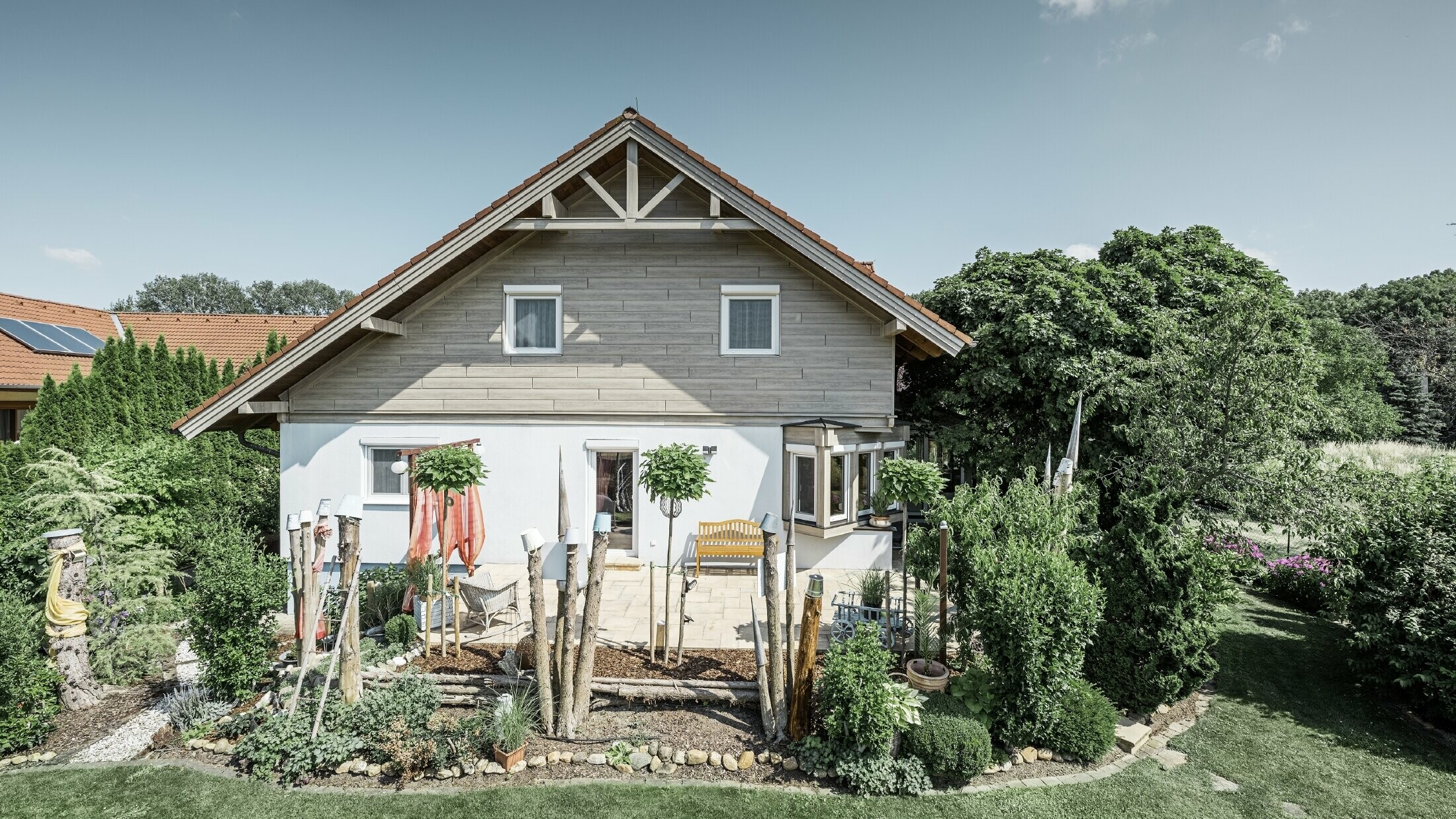 Samostojeća kuća s obnovljenom pročeljem, novom oblogom krova u modernoj sivo-bež završnici s efektom drva, kombiniranom s malterisanim pročeljem, krovom sa dvovodnim krovnim pokrovom i uređenim vrtom.