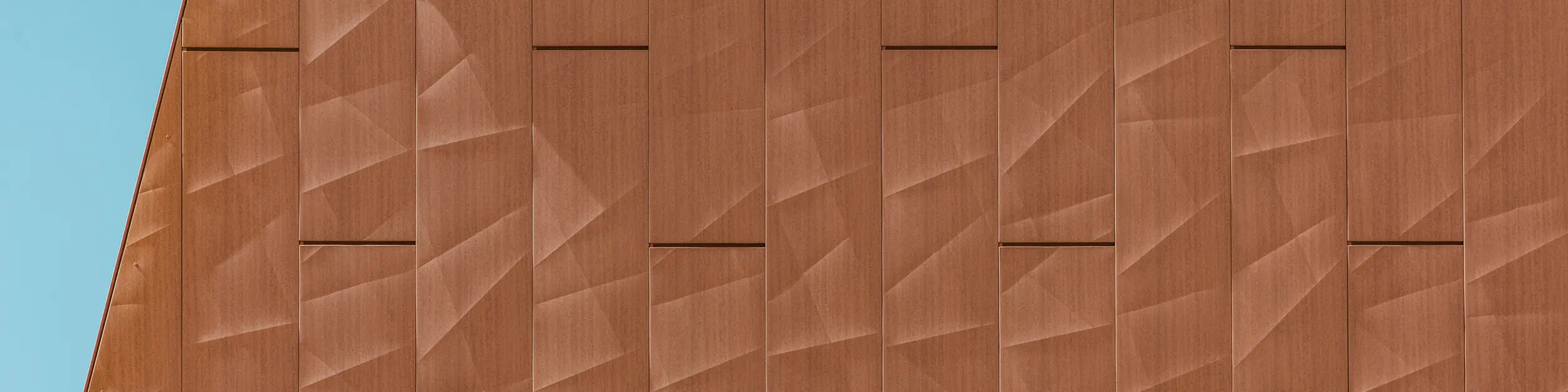 Detaljni prikaz PREFA Siding.X aluminijske fasade na postrojenju za pitku vodu WML u Lottumu s precizno oblikovanim panelima u toplom izgledu hrđe kao vizualnim atraktivnim elementom. Geometrijski strukturirana površina stvara fascinantnu igru svjetla, sjene i finih linija koja se, ovisno o kutu gledanja, živahno mijenja. Visokokvalitetni PREFA aluminijski paneli odlikuju se malom težinom, visokom otpornošću na vremenske uvjete, postojanošću boje i potpunom mogućnošću recikliranja – za dugotrajno, održivo i jednostavno održavanje fasadno rješenje.