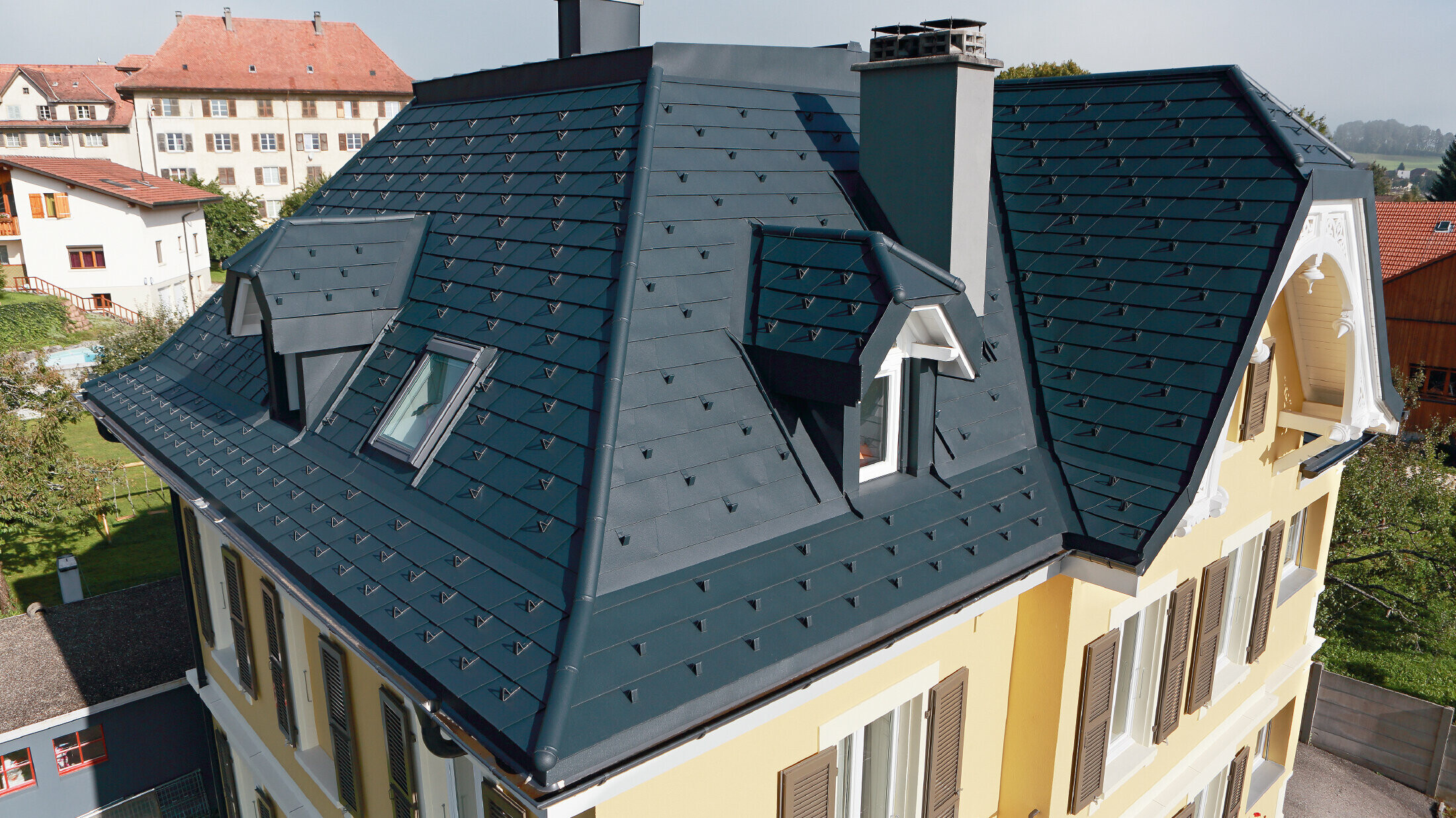 Vila u Švicarskoj, krov ima brojne upuštene uvale i male krovne kućice, krov je pokriven aluminijskom šindrom tvrtke PREFA u P.10 antracit boji.