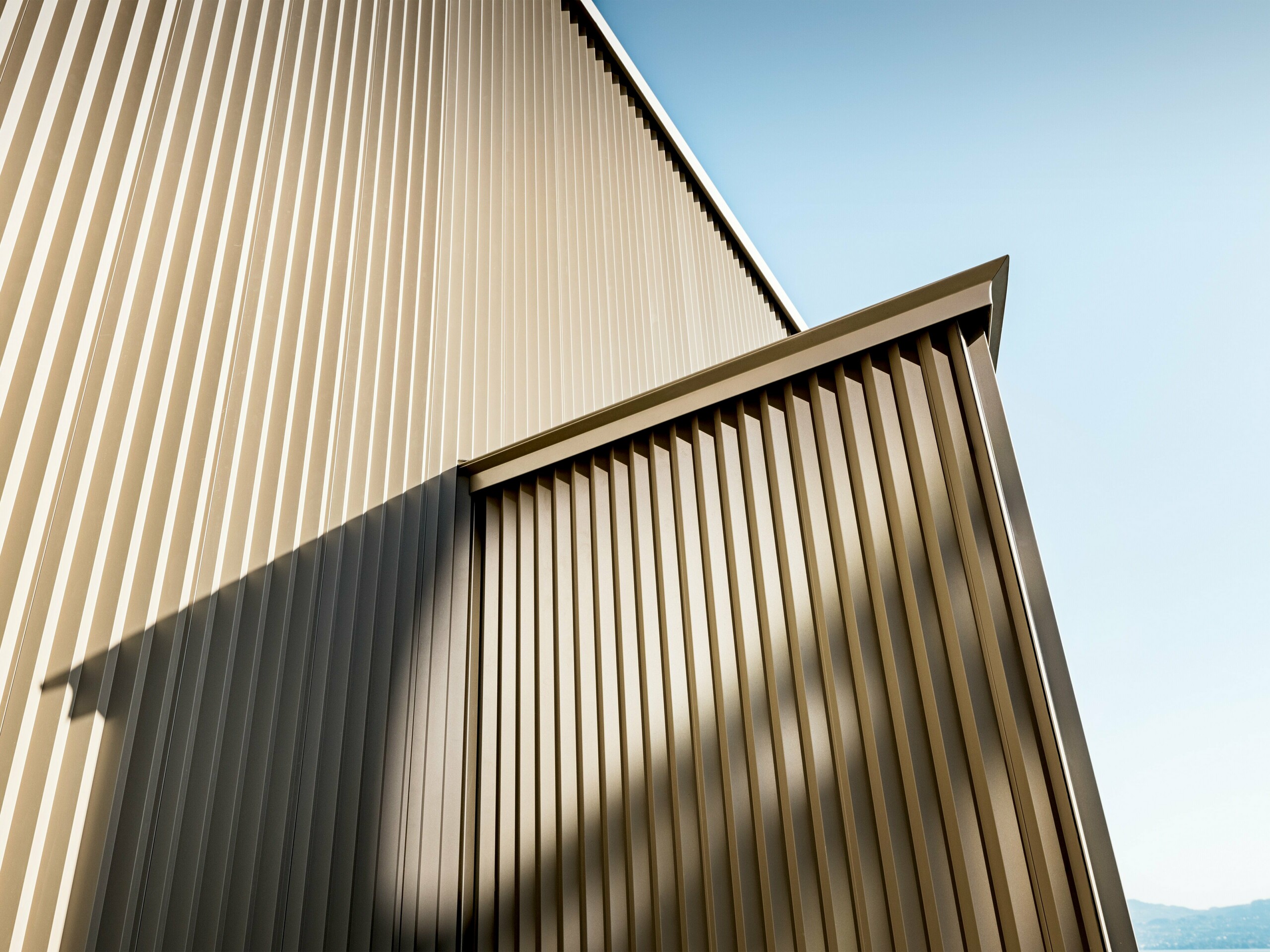 Elegantna PREFA aluminijska fasada u brončanoj nijansi na stambenoj kući u St. Gingolphu, koju je dizajnirala arhitektica Sophie Morard. Vertikalno zupčasti individualni profili stvaraju fascinantnu igru svjetla, sjene i teksture, dajući fasadi dubinu i dinamiku. Kvalitetna, praškasto premazana površina osigurava dugotrajnu zaštitu i elegantnu estetiku – idealno za zahtjevne stambene projekte. Brončani sjaj fasade skladno se uklapa u alpski okoliš, čineći malu kuću arhitektonskim biserom s velikim vizualnim učinkom.