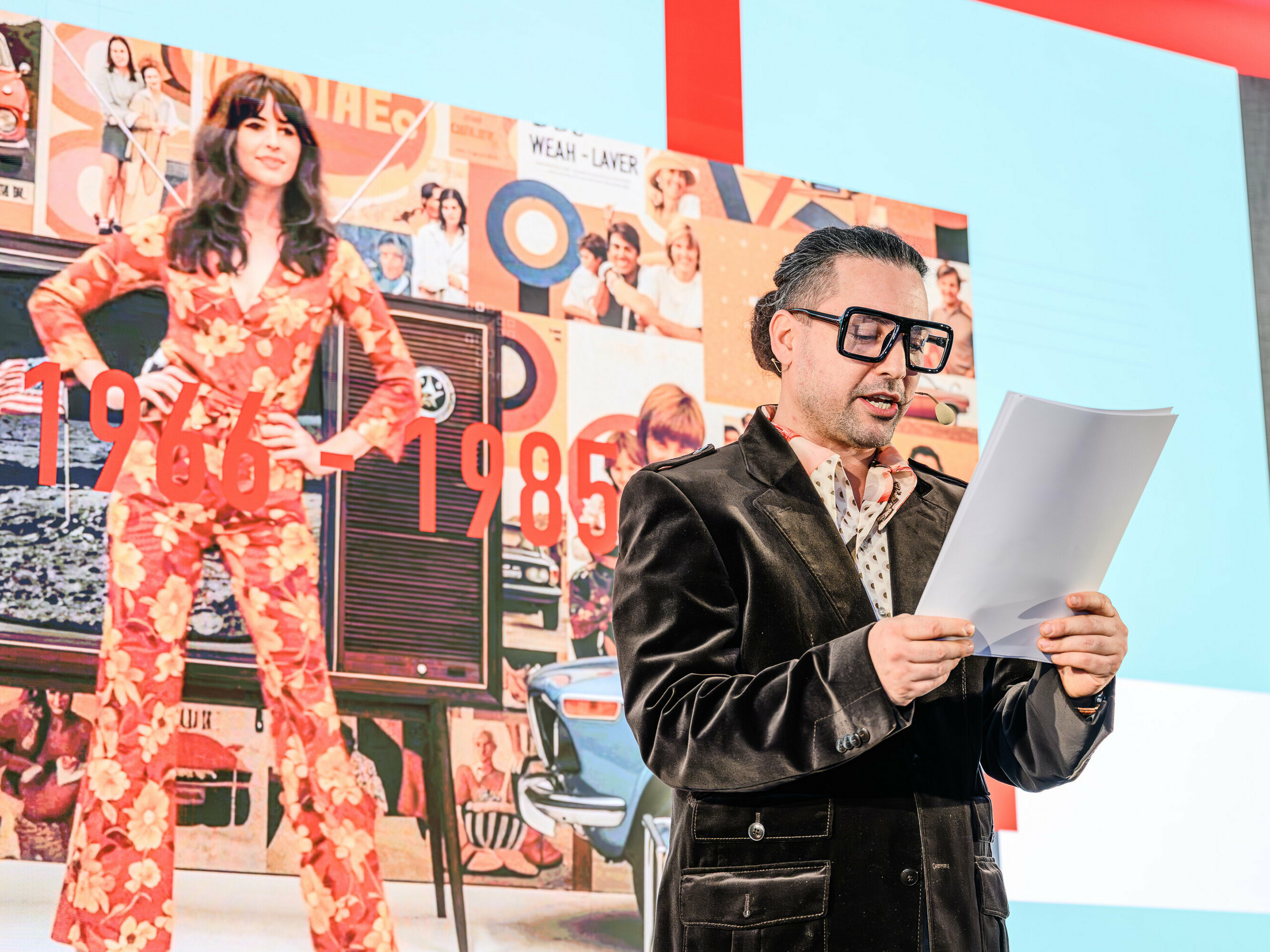 Putovanje kroz vrijeme na pozornici PREFARENZEN prezentacije 2026.: karizmatični Serkan Temel u retro izdanju vodi publiku kroz desetljeća. U fokusu su godine od 1966. do 1985., prikazane na kolažu u pozadini s dizajnerskim ikonama i društvenim trendovima tog razdoblja. Baš kao što PREFA proizvodi nadmašuju trendove stilom i sadržajem, prezentacija pokazuje kako arhitektura jučer postaje inspiracija za rješenja sutra – ponovno interpretirana aluminijem.