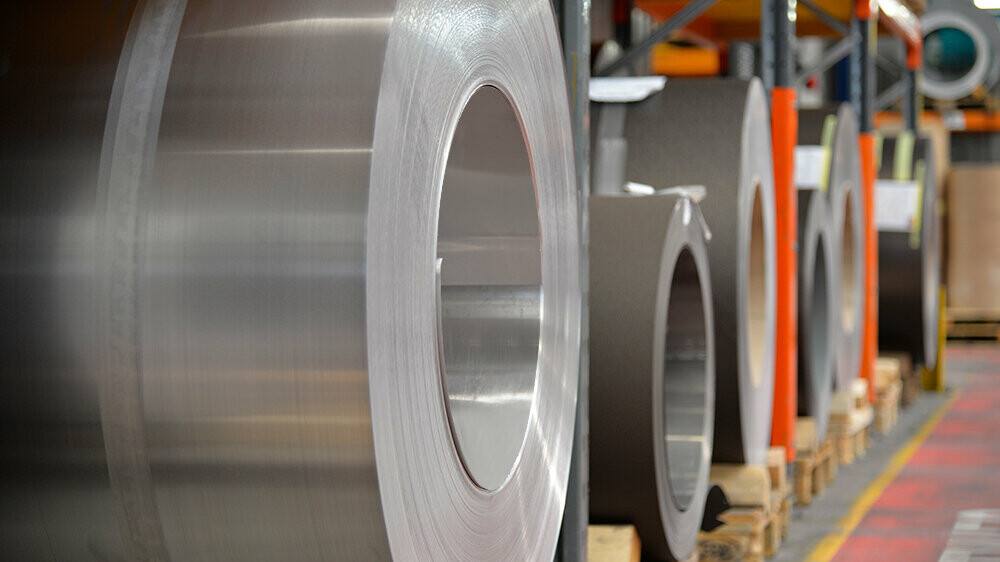 Koluti aluminija (coils) položeni na drvenim paletama, u fokusu je kolut aluminija u natur boji, a iza njega nalaze se dodatne trake i limovi od aluminija.