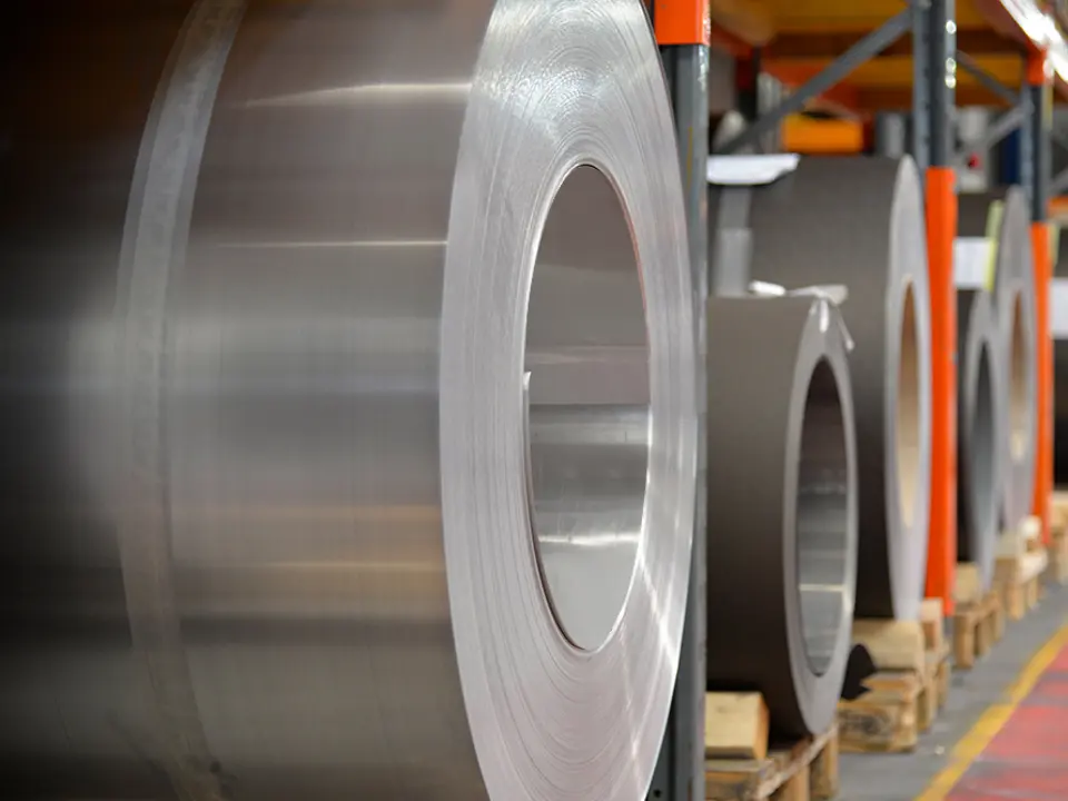Koluti aluminija (coils) položeni na drvenim paletama, u fokusu je kolut aluminija u natur boji, a iza njega nalaze se dodatne trake i limovi od aluminija.