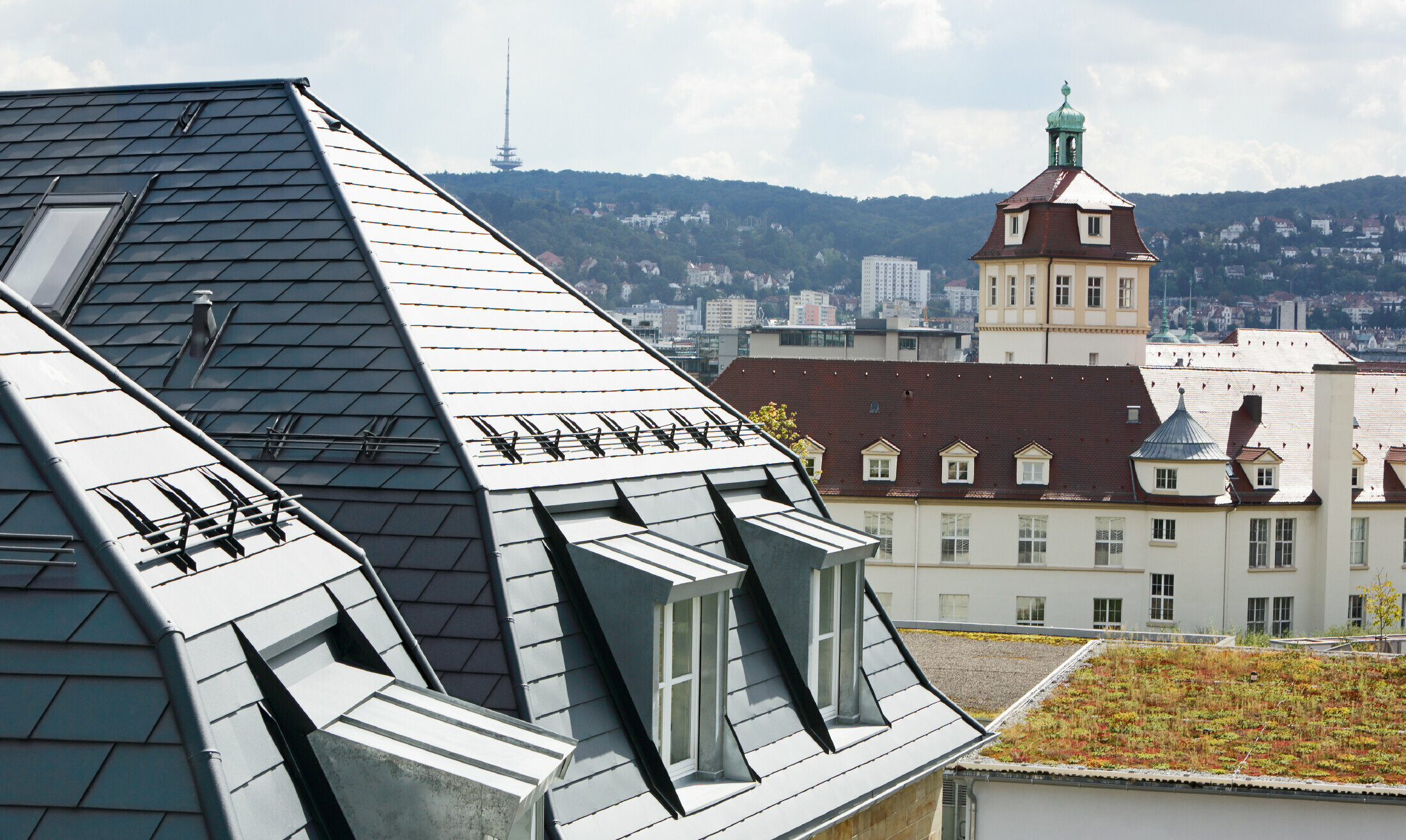 Stara gradska kuća u Stuttgartu s nakrivljenim krovom i brojnim krovnim kućicama s prozorima, pokrivena aluminijskom šindrom tvrtke PREFA u P.10 antracit boji