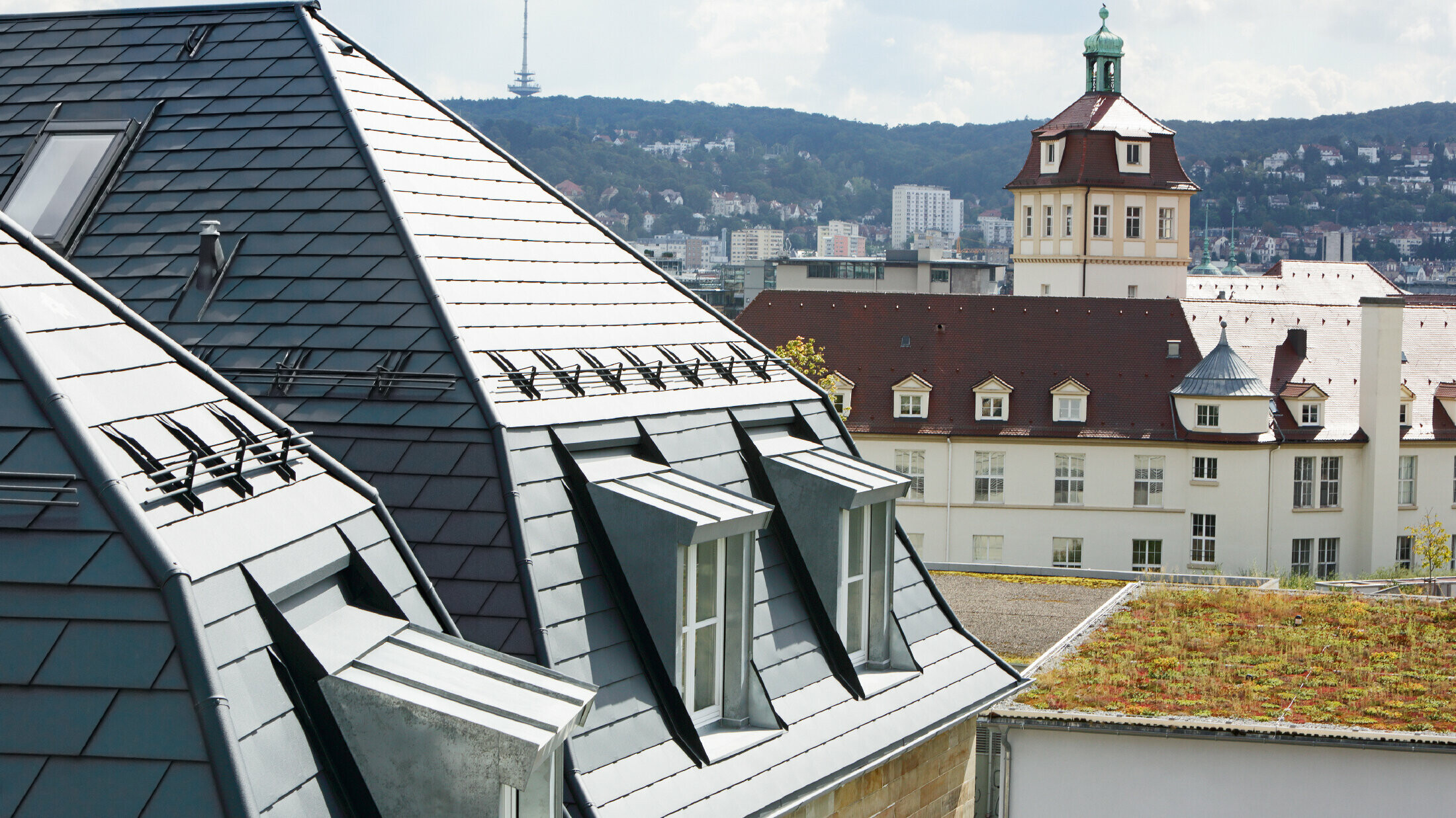 Stara gradska kuća u Stuttgartu s nakrivljenim krovom i brojnim krovnim kućicama s prozorima, pokrivena aluminijskom šindrom tvrtke PREFA u P.10 antracit boji